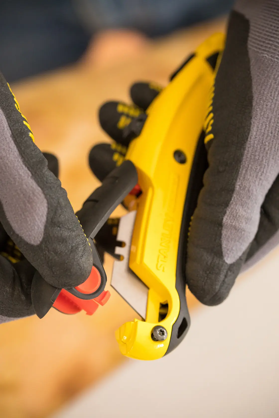 STANLEY 7-10-778 yellow utility knife held by gloved hands, close-up showing blade area.
