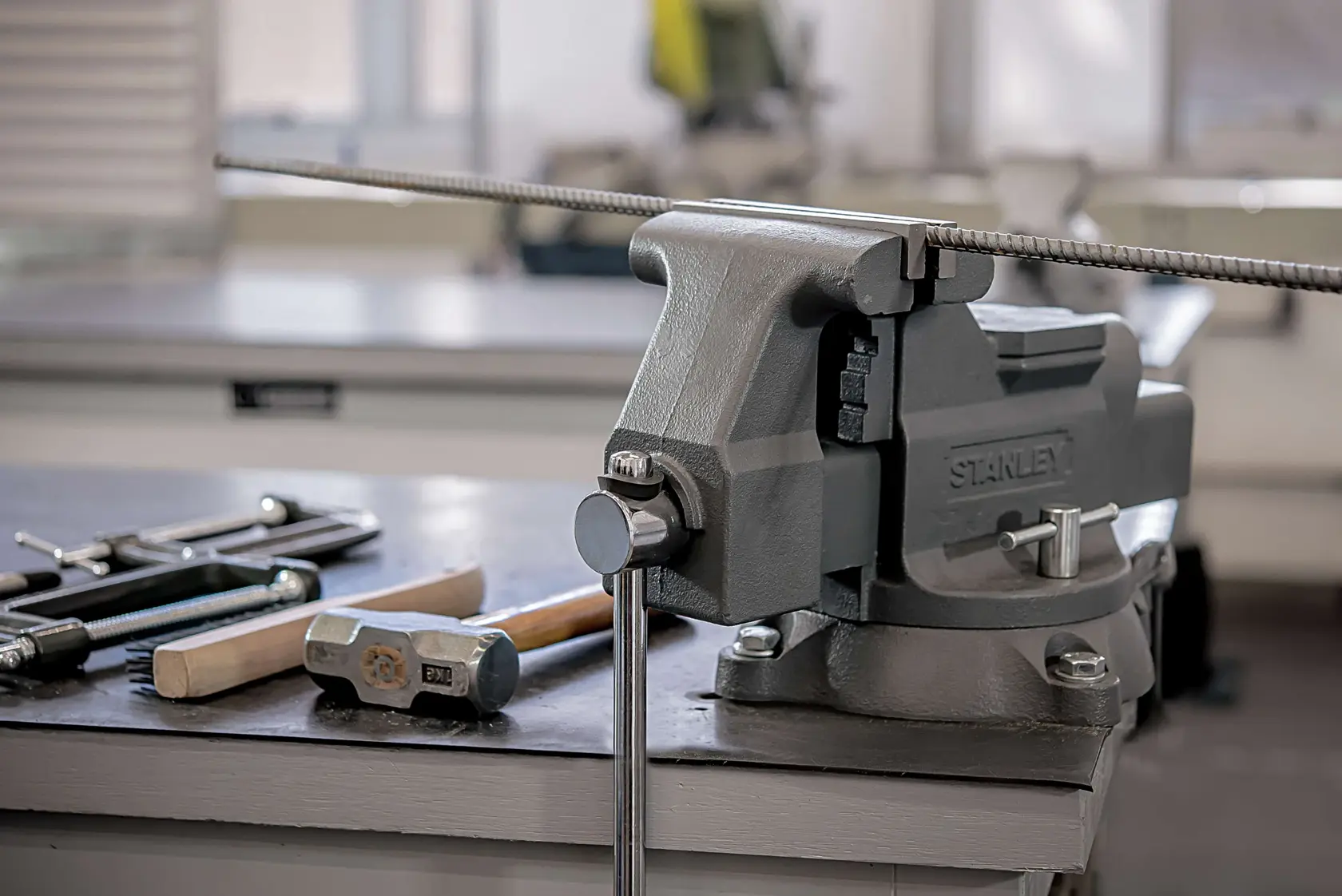 Photo of STANLEY 83-066 bench vise mounted on workbench, holding metal rod, with tools beside it.