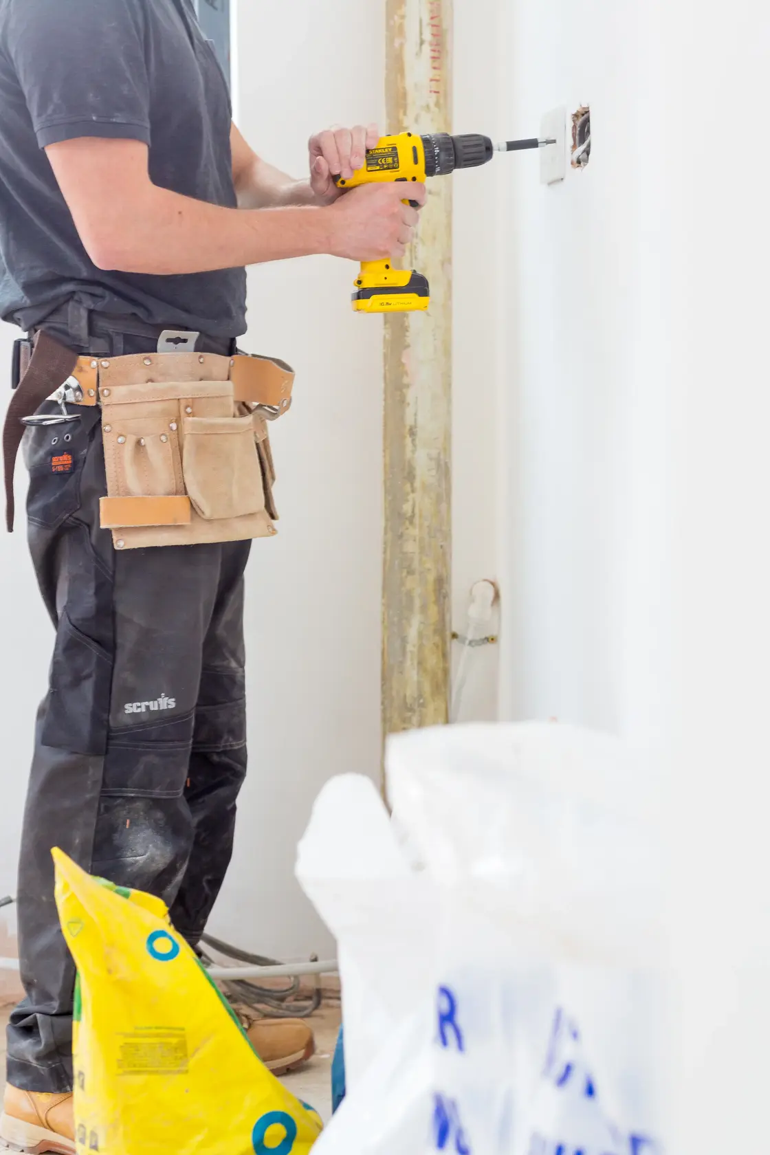 STANLEY FMC021S2 cordless drill used by worker installing outlet, indoor close-up, tool belt visible.