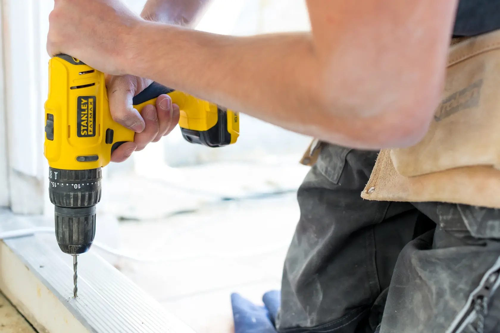 Photo of STANLEY FMC021S2 cordless drill in use, yellow body, drilling into metal surface, close-up view.