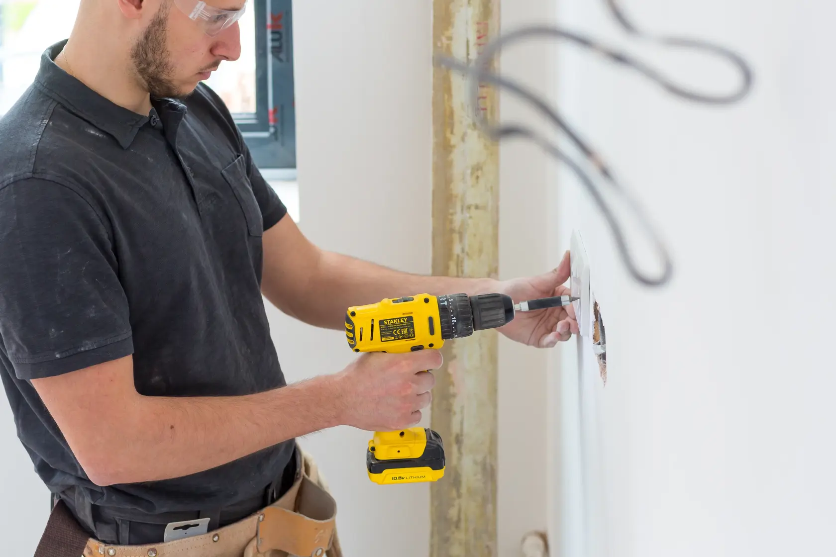 STANLEY FMC021S2 cordless drill used by person installing in wall, yellow and black design, side view.
