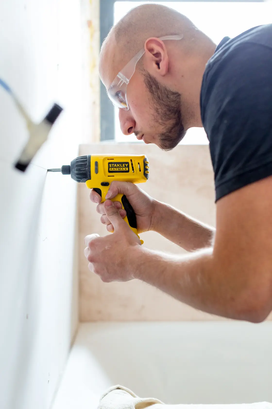 Stanley FMC041S2 cordless drill used on a wall, close-up view showing yellow and black tool in action.