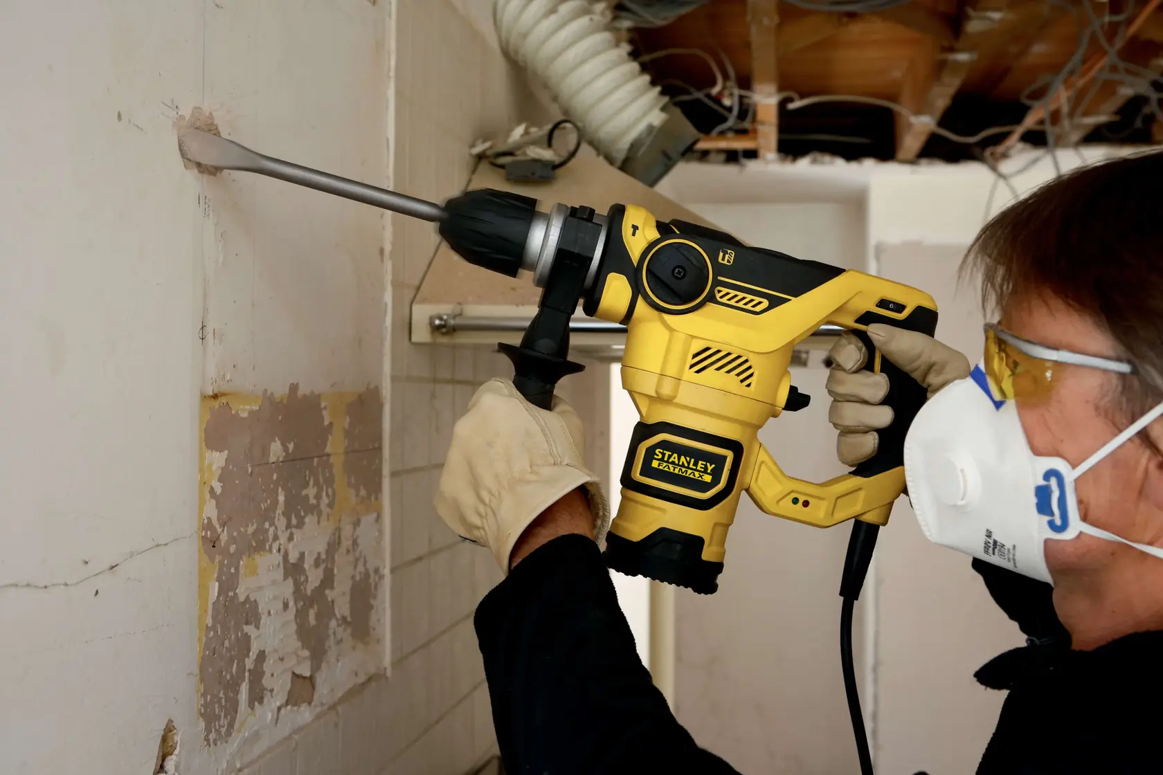 Photo of person using STANLEY FME1250K rotary hammer, drilling into wall, with gloves and safety mask.