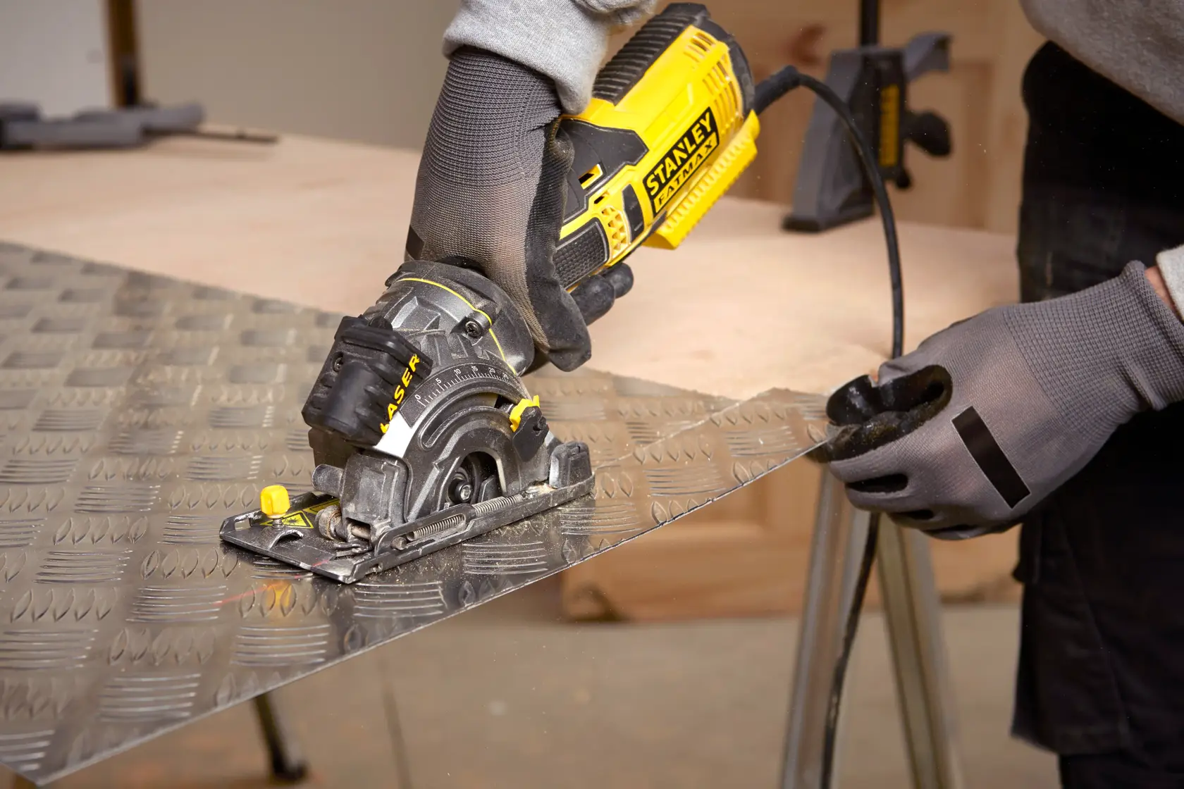 STANLEY FME380K compact circular saw cutting metal sheet, close-up with gloved hands, workshop setting.