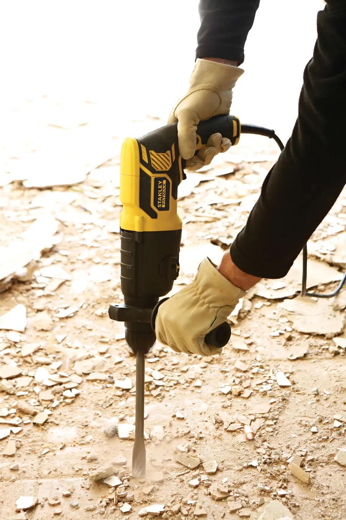 STANLEY FME500K demolition hammer in use on debris-covered floor, worker wearing gloves.