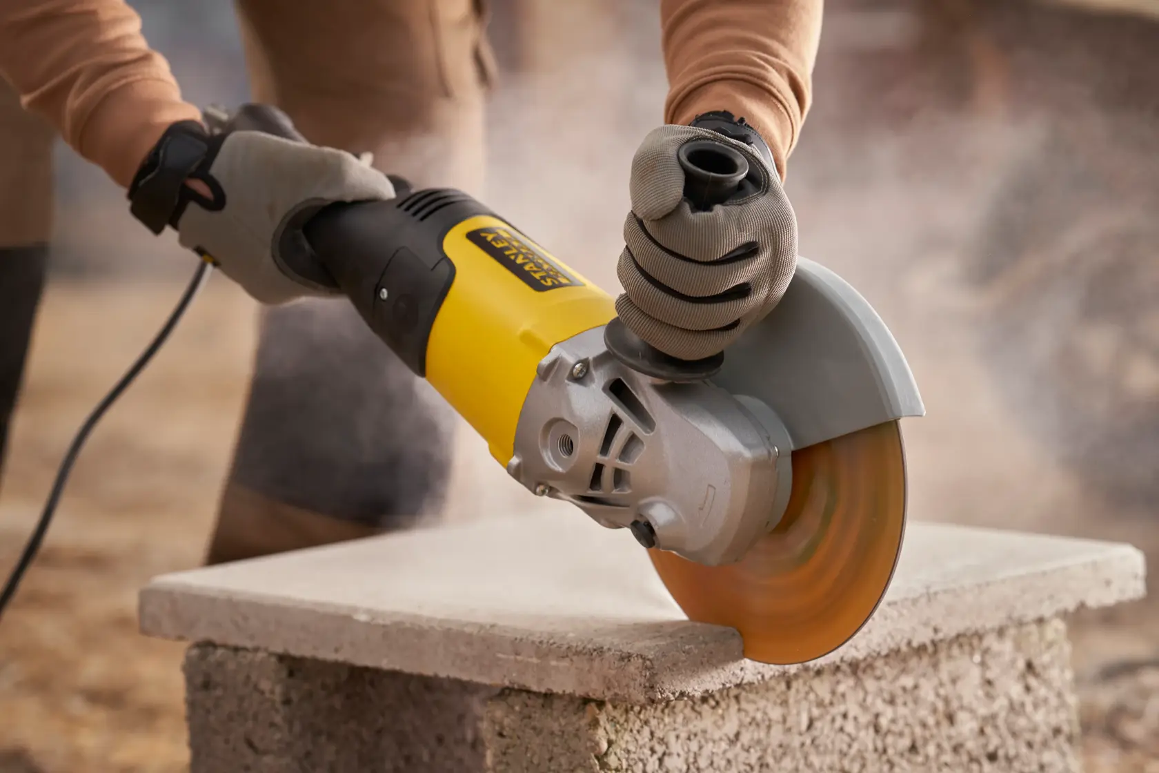 STANLEY FMEG232 angle grinder in use cutting concrete block, close-up view.