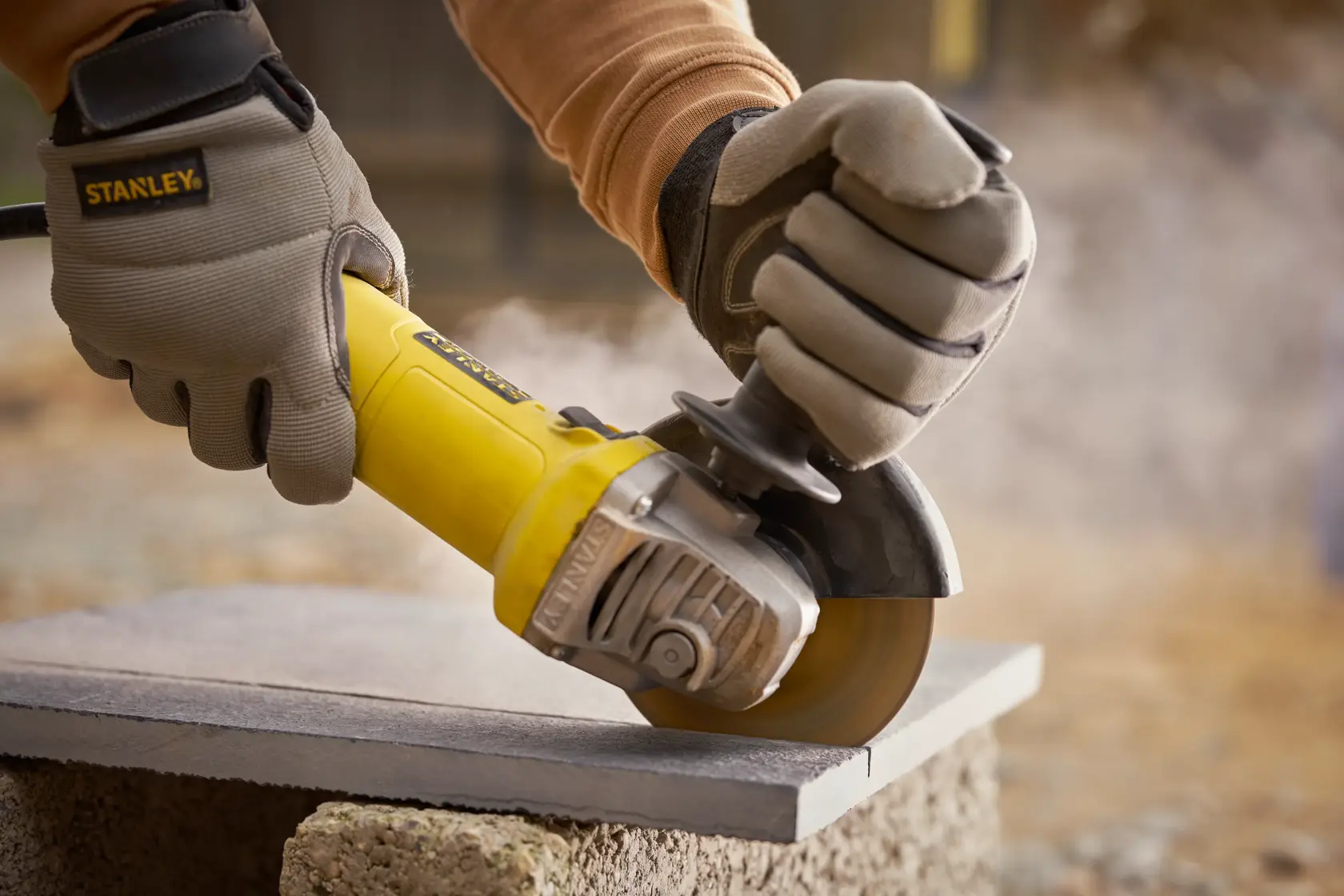 STANLEY FMEG615 angle grinder in use, cutting stone, close-up with work gloves.