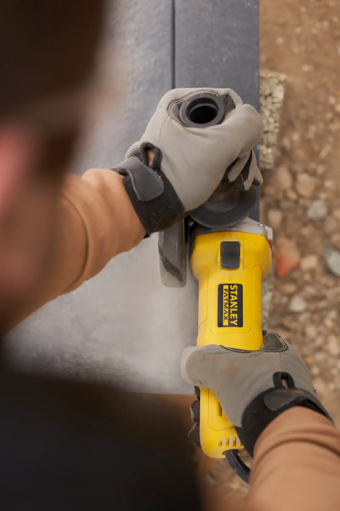Photo of STANLEY FMEG615 angle grinder in use, worker wearing gloves, grinding metal surface.