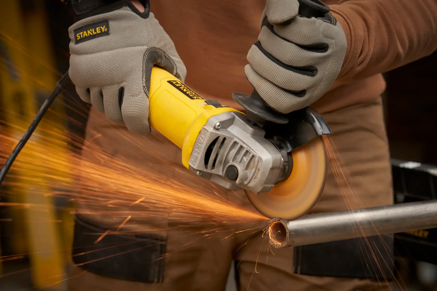 STANLEY FMEG615 angle grinder cutting metal pipe with sparks, close-up action shot.