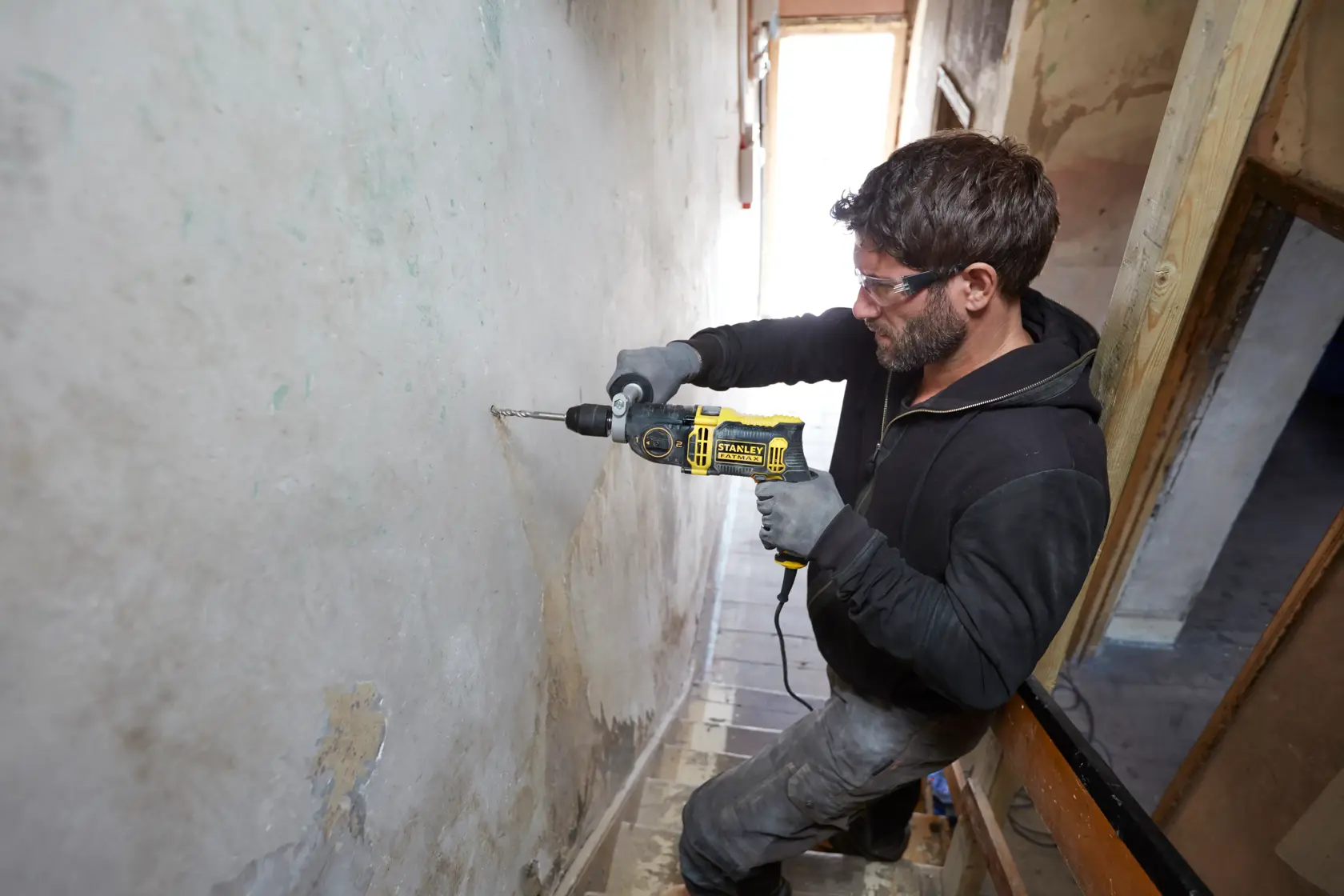 Stanley FMEH1100K corded drill in use drilling into wall, product photography, side angle.