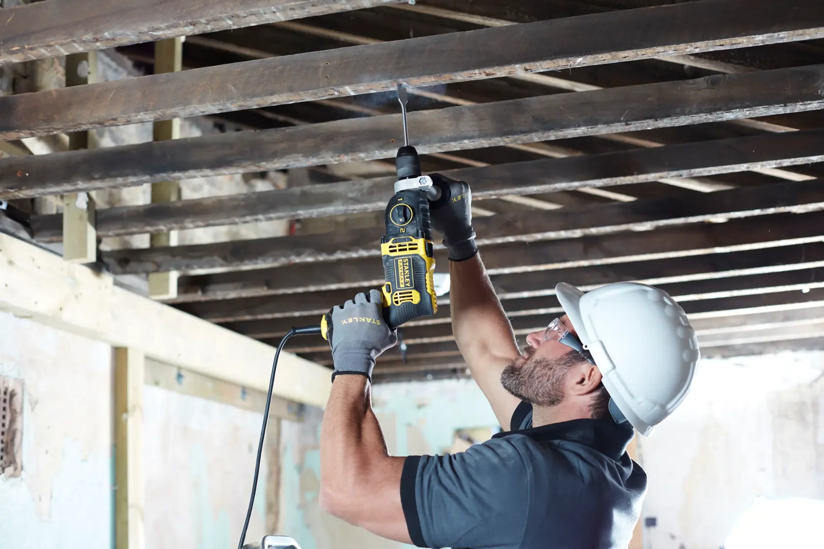 Photo of worker using STANLEY FMEH850K corded drill to bore upwards into wood beams, wearing safety gear.