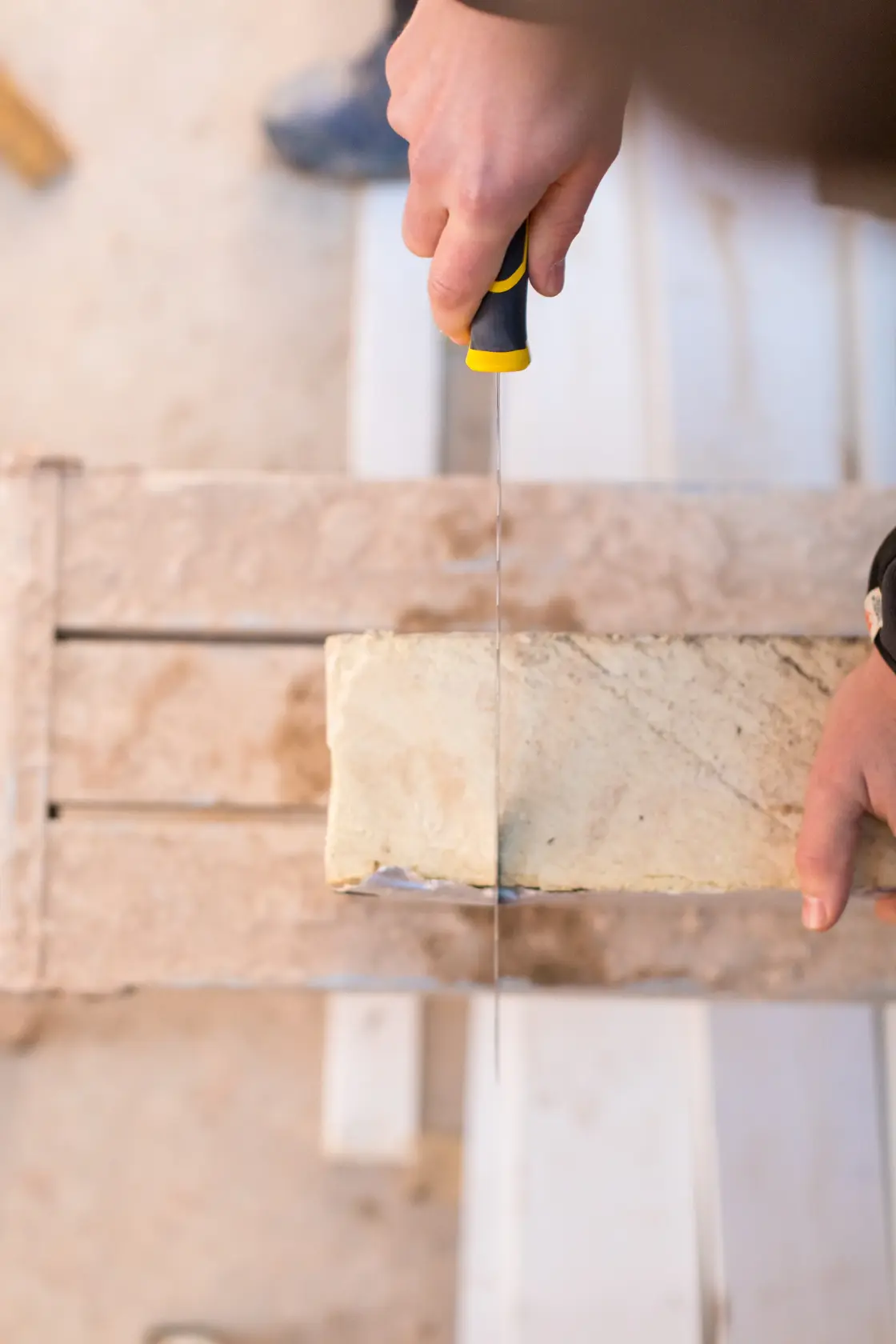 STANLEY FMHT0-10327 hand saw cutting a beige brick, top-down angle, construction setting.