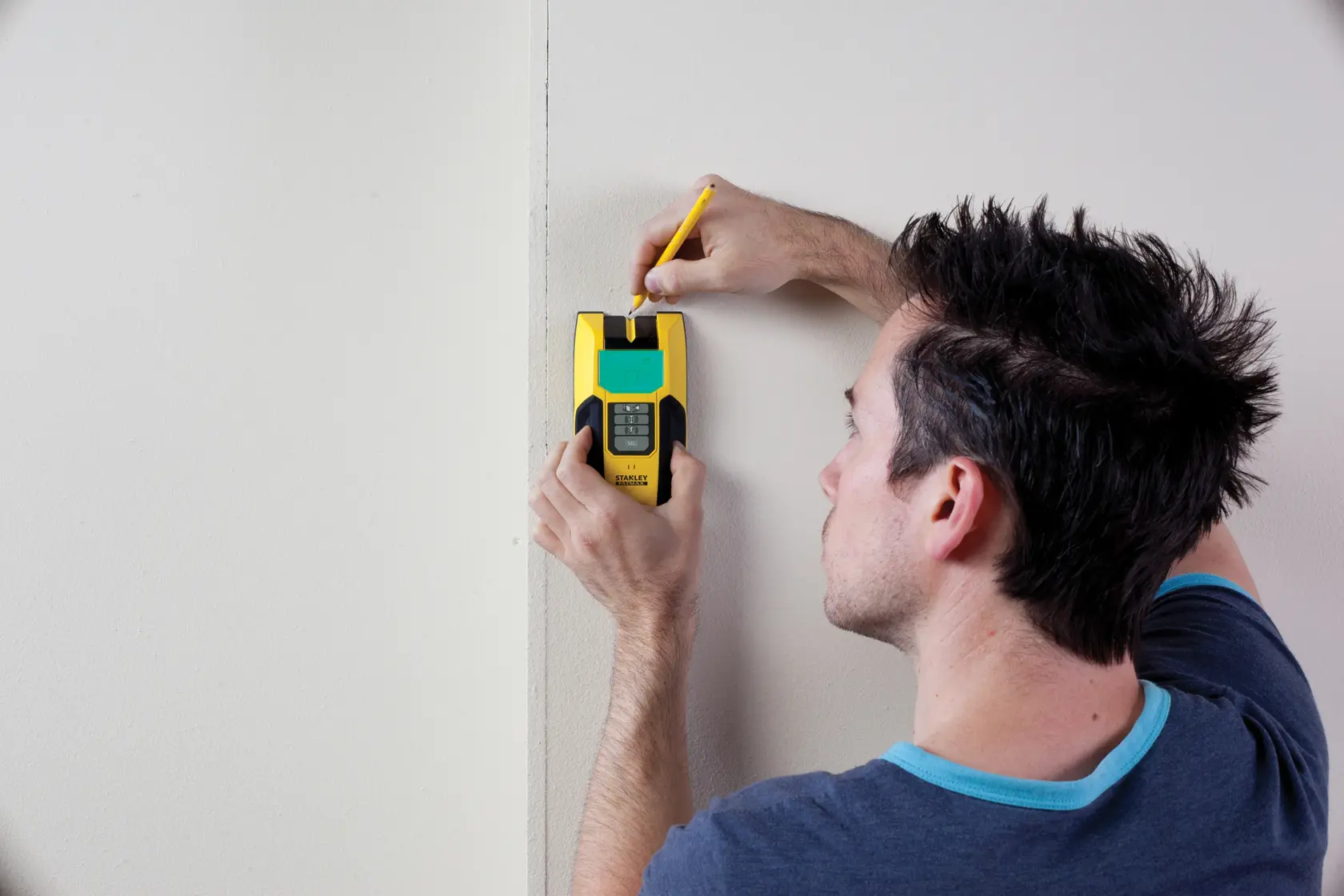 STANLEY FMHT0-77407 stud finder used on wall, user marking with pencil, yellow and black handheld device.