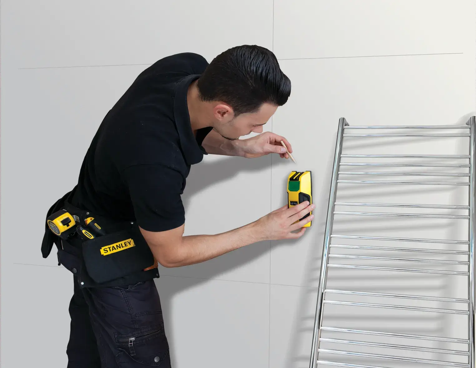 STANLEY FMHT0-77407 wall scanner tool in use by a person marking a wall near a metal ladder.