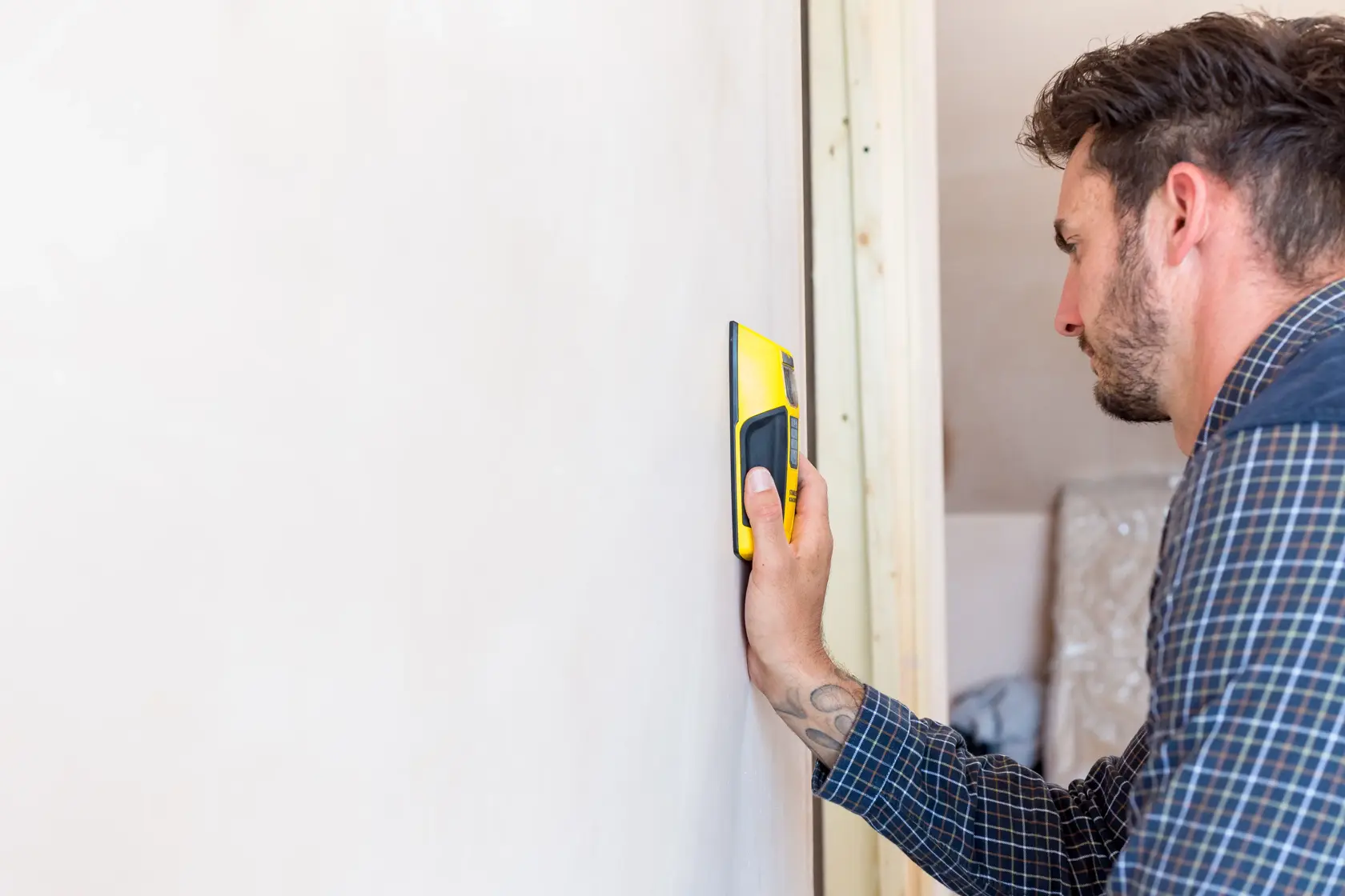 STANLEY FMHT0-77407 stud finder in hand detecting wooden stud in wall, side view, home interior.