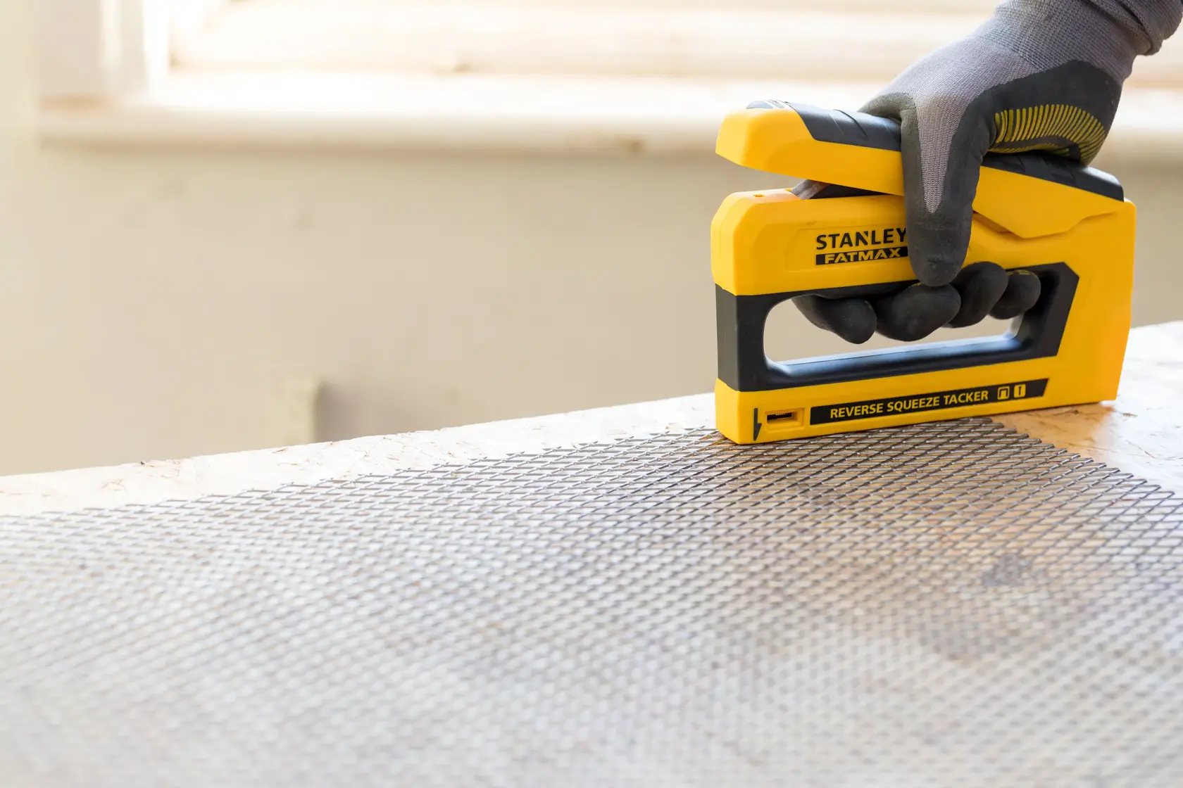 Stanley FMHT0-80551 stapler being used on wire mesh, close-up angle, yellow and black design.