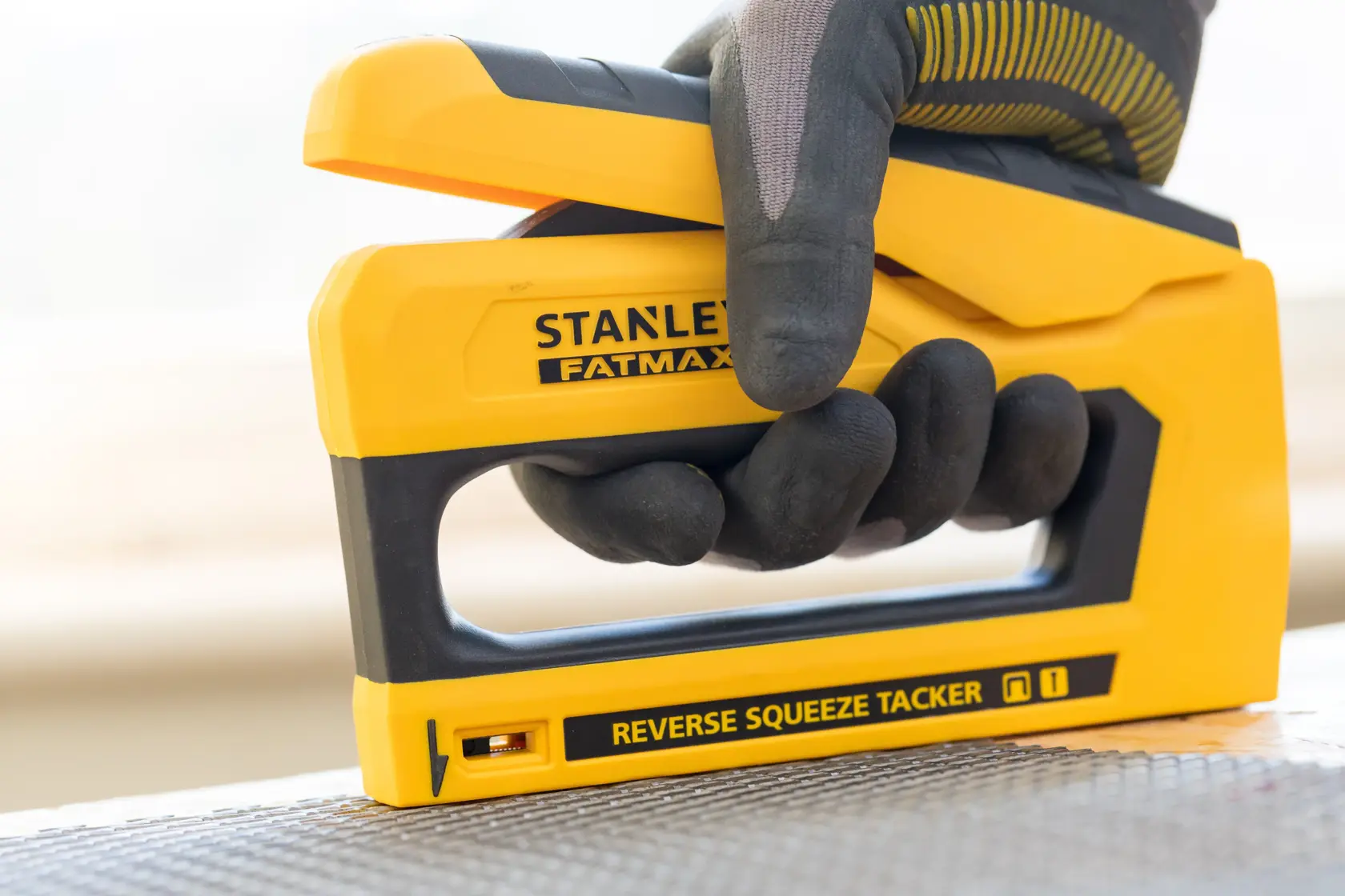 Photo of STANLEY FMHT0-80551 stapler, yellow and black, being used with a gloved hand on a surface.