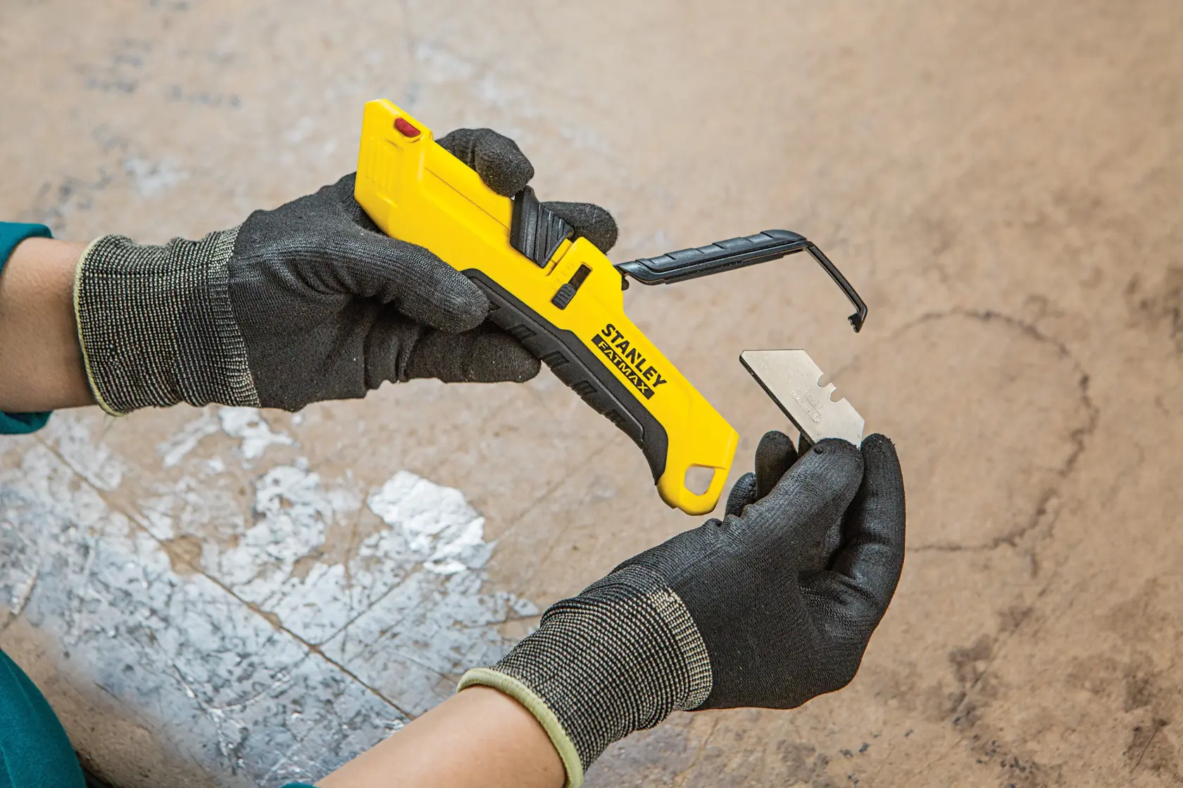 Photo of STANLEY FMHT10365-0 utility knife with yellow handle and blade being replaced by gloved hands.