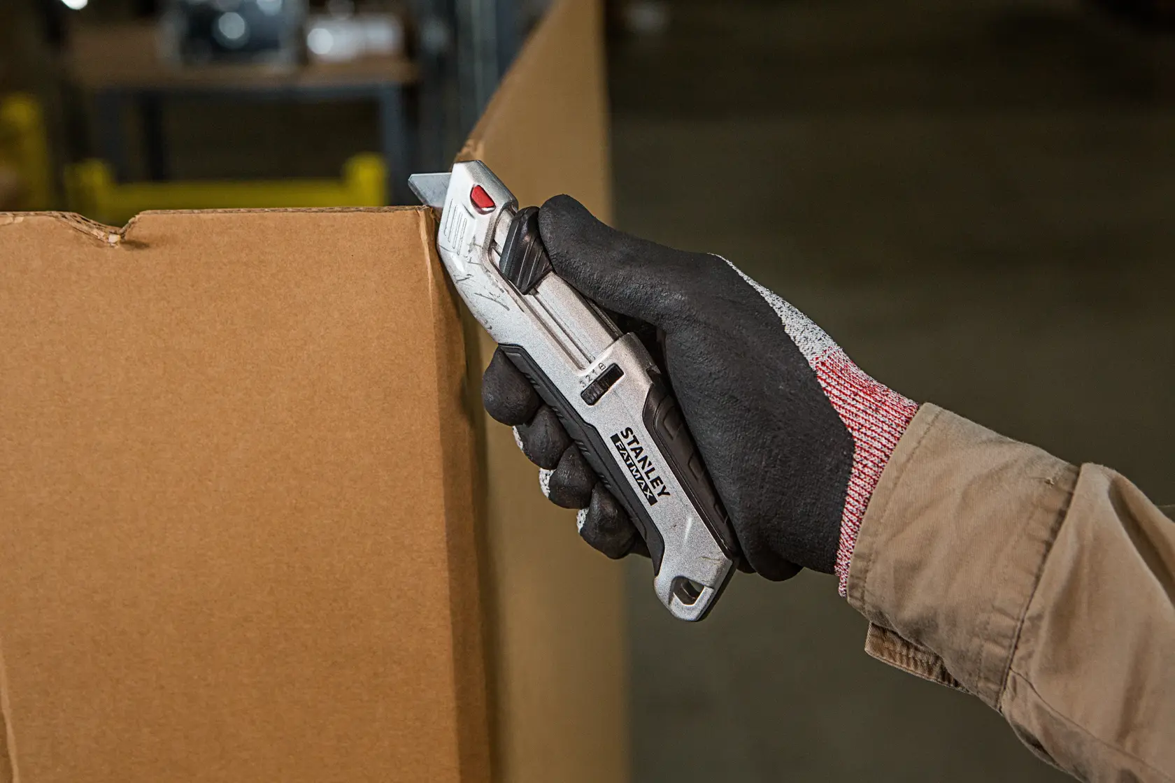 Stanley FMHT10367-0 utility knife cutting cardboard, held in gloved hand, product in use.