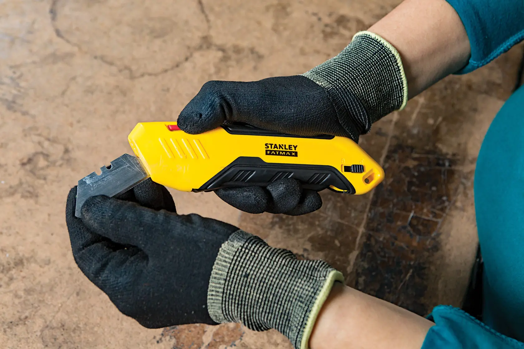 Stanley FMHT10369-0 utility knife with yellow and black handle, held by gloved hands, side view.