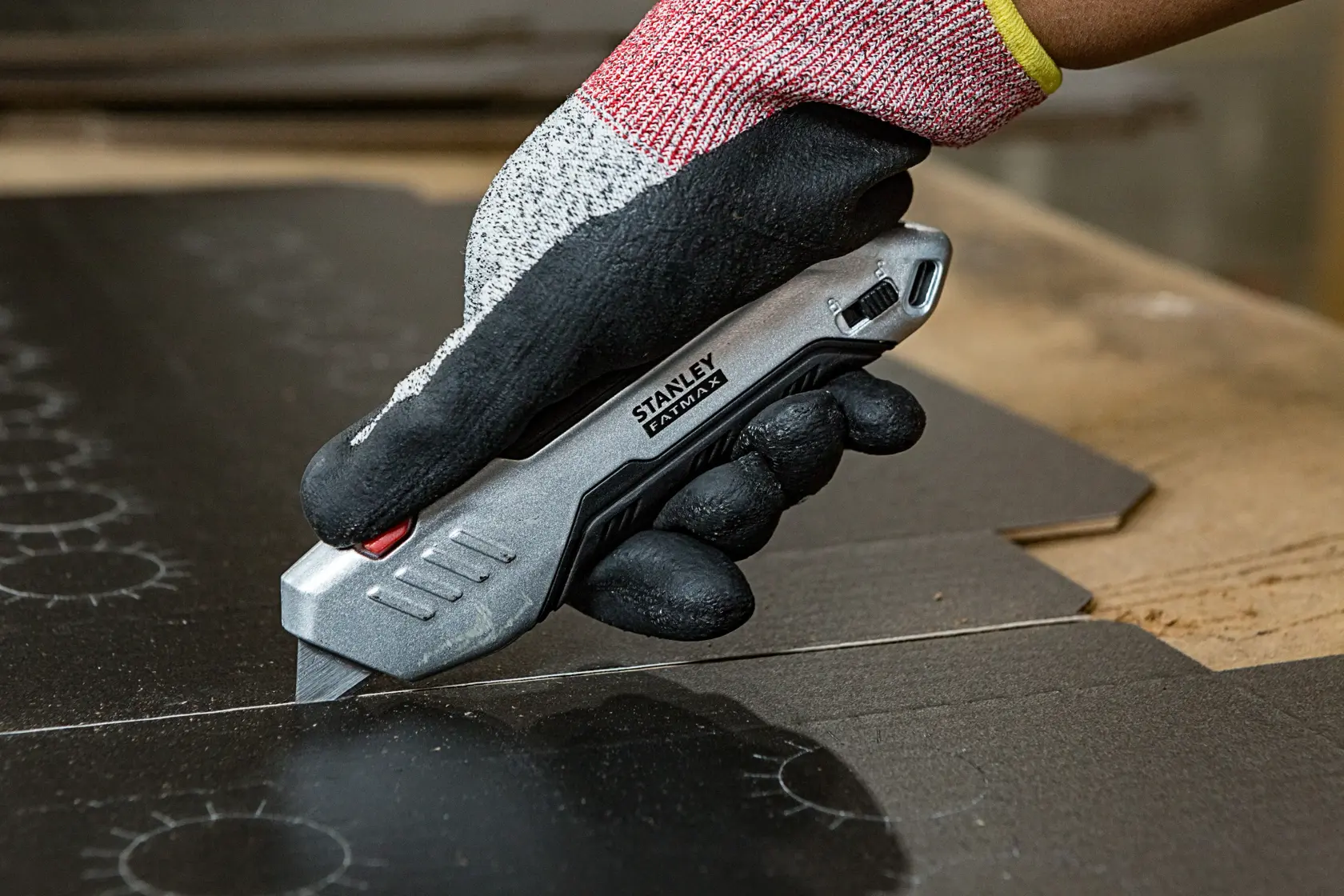 STANLEY FMHT10370-0 utility knife cutting cardboard, held by gloved hand, close-up photo.
