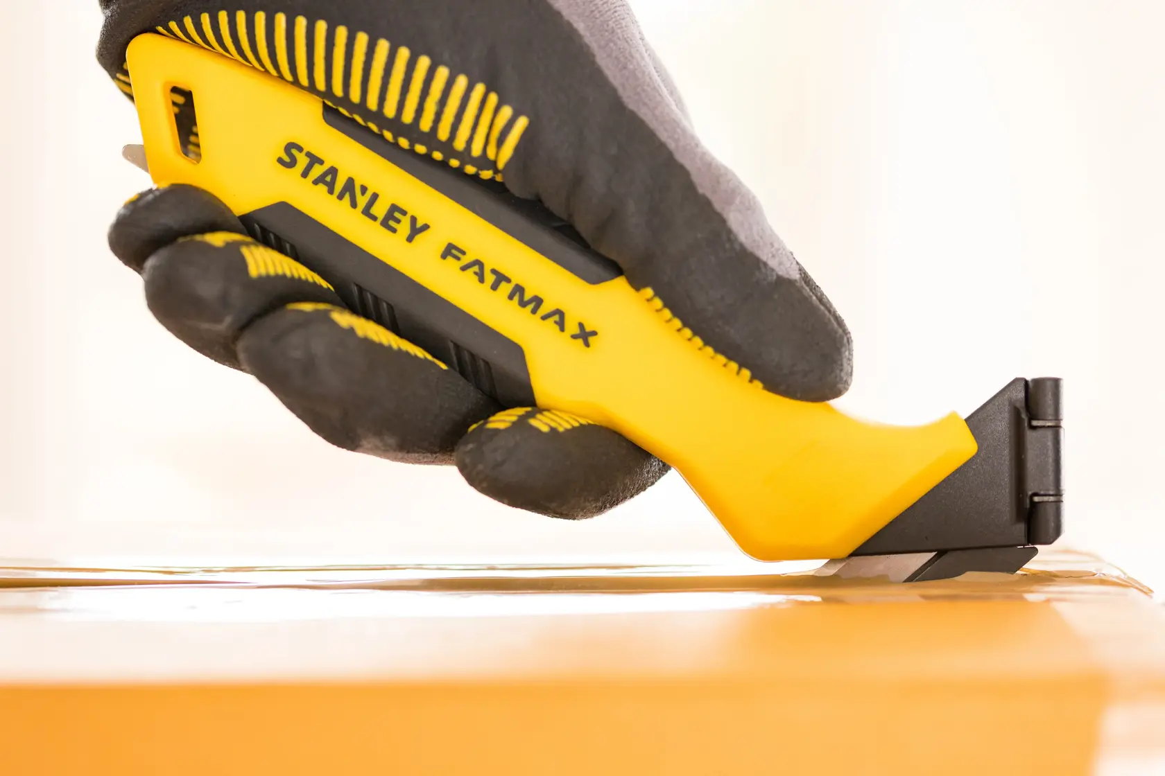 Photo of STANLEY FMHT10373-0 utility knife in a gloved hand, cutting tape on a cardboard box.