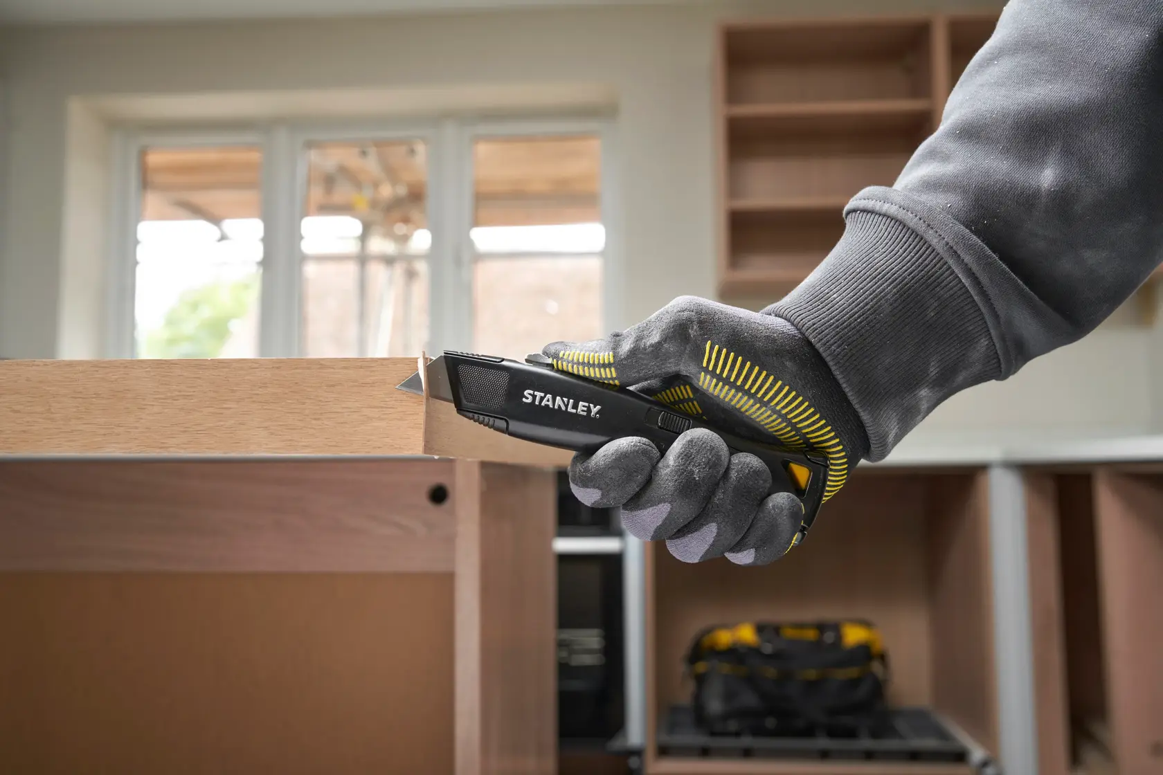 STANLEY FMHT10504-0 utility knife in gloved hand cutting wood, indoor setting, product side view.