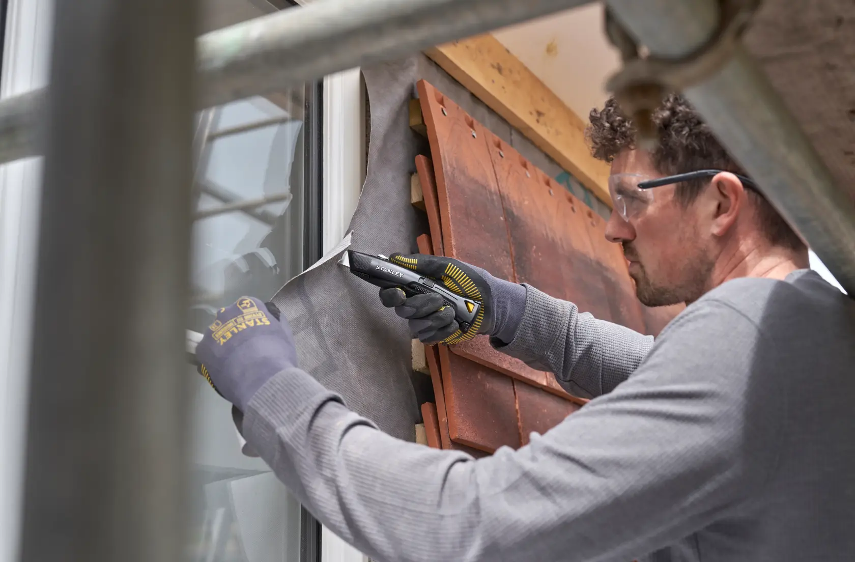 STANLEY FMHT10504-0 utility knife in use cutting building wrap near window, close-up during construction work.