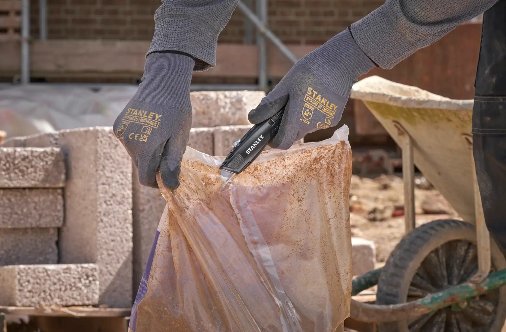 Photo of worker using STANLEY FMHT10504-0 utility knife to open a plastic bag on a construction site.