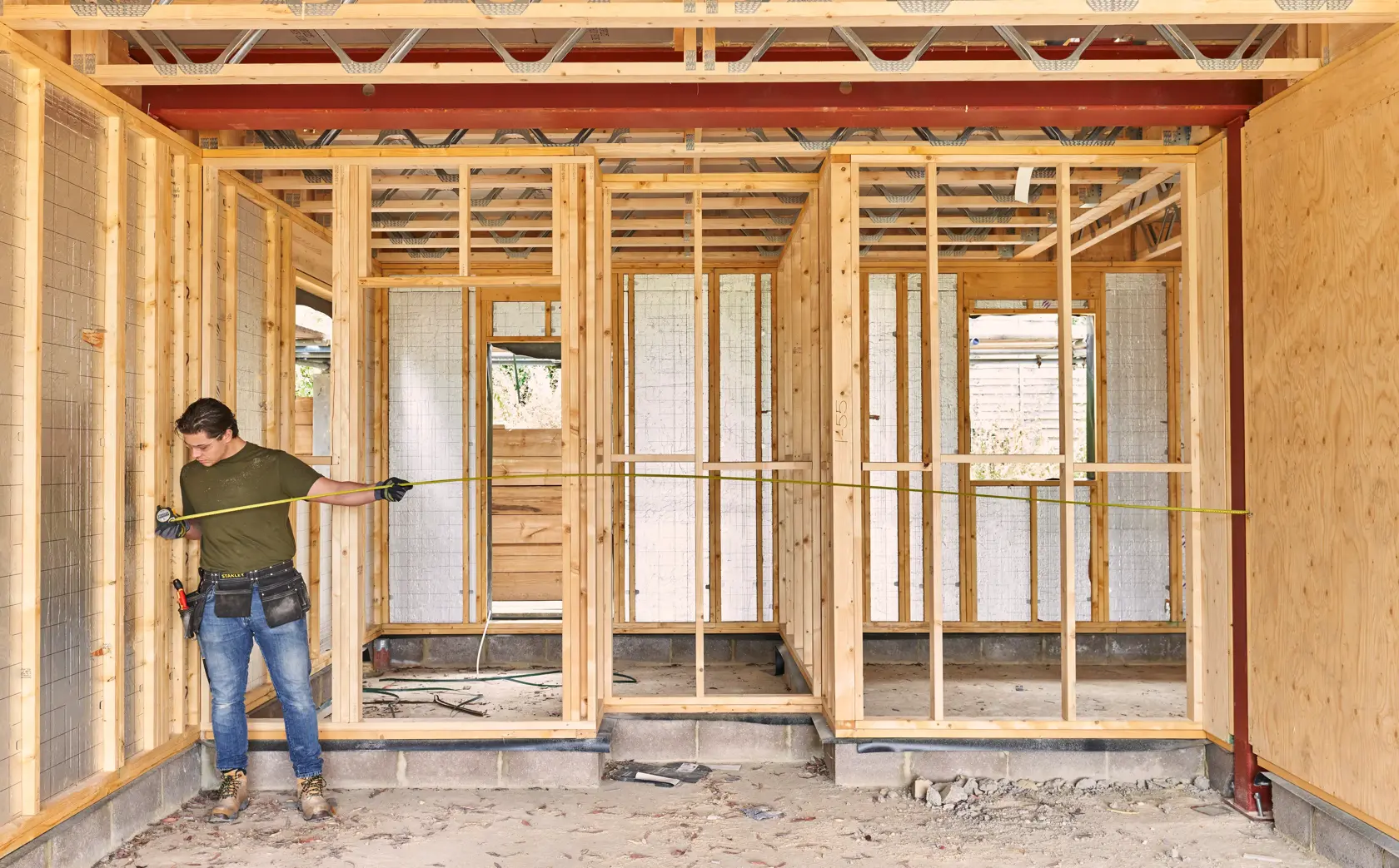 STANLEY FMHT38214-0 tape measure in use at construction site, worker measuring wooden frame.