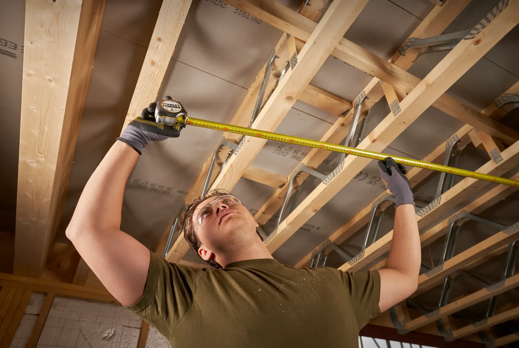 STANLEY FMHT38214-0 tape measure used to measure wooden ceiling beams in a construction interior.