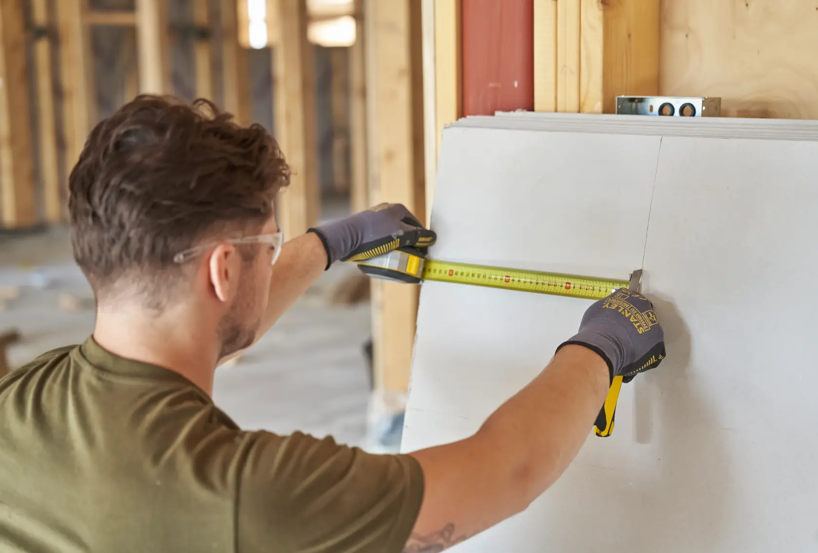 Photo of person using STANLEY FMHT38214-0 tape measure, measuring drywall panel indoors on construction site.
