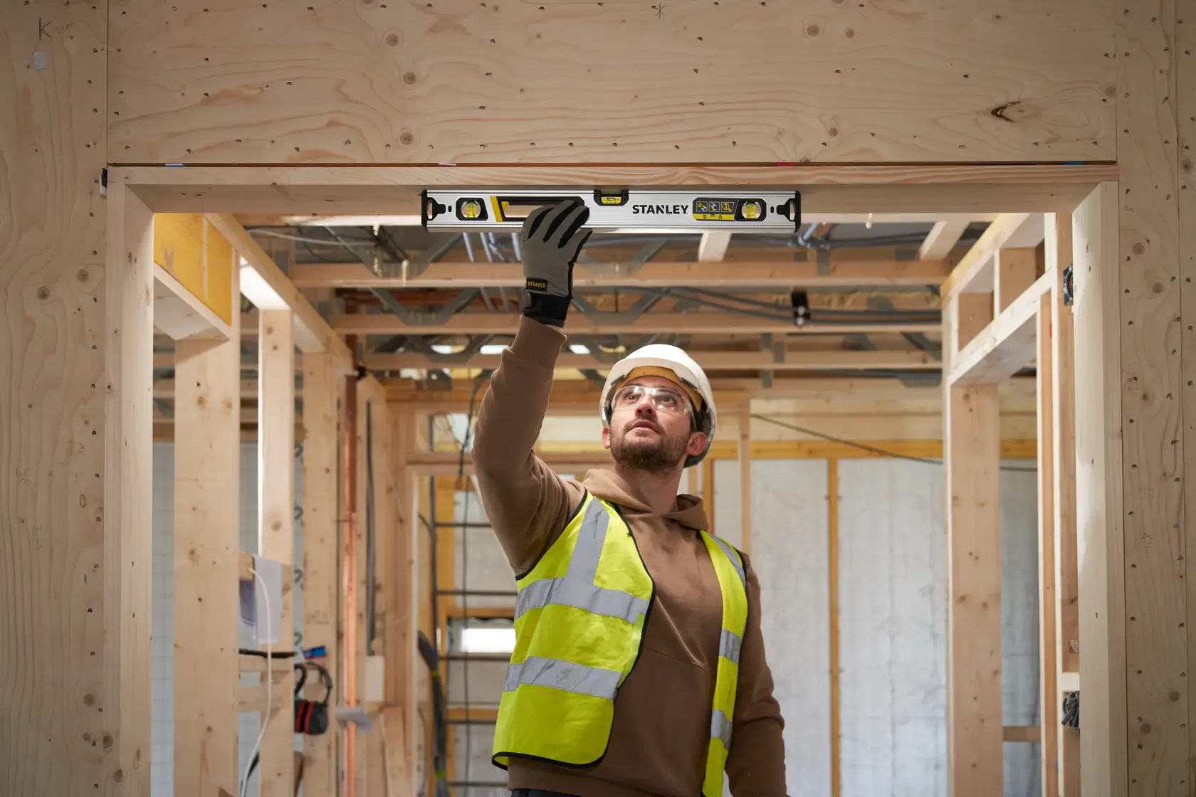 STANLEY FMHT43672 spirit level held by worker checking alignment in wooden construction site.