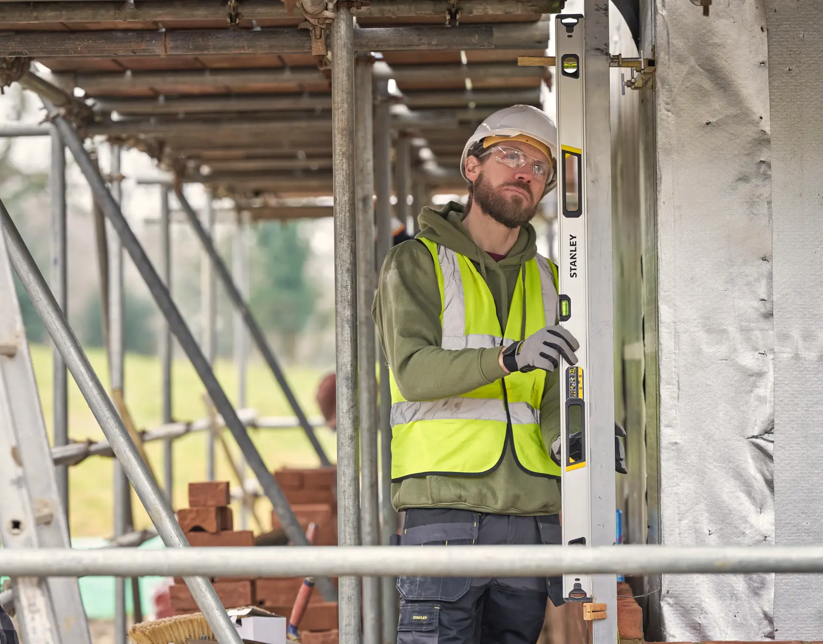 STANLEY FMHT43677 spirit level used by worker in high-visibility vest at construction site.