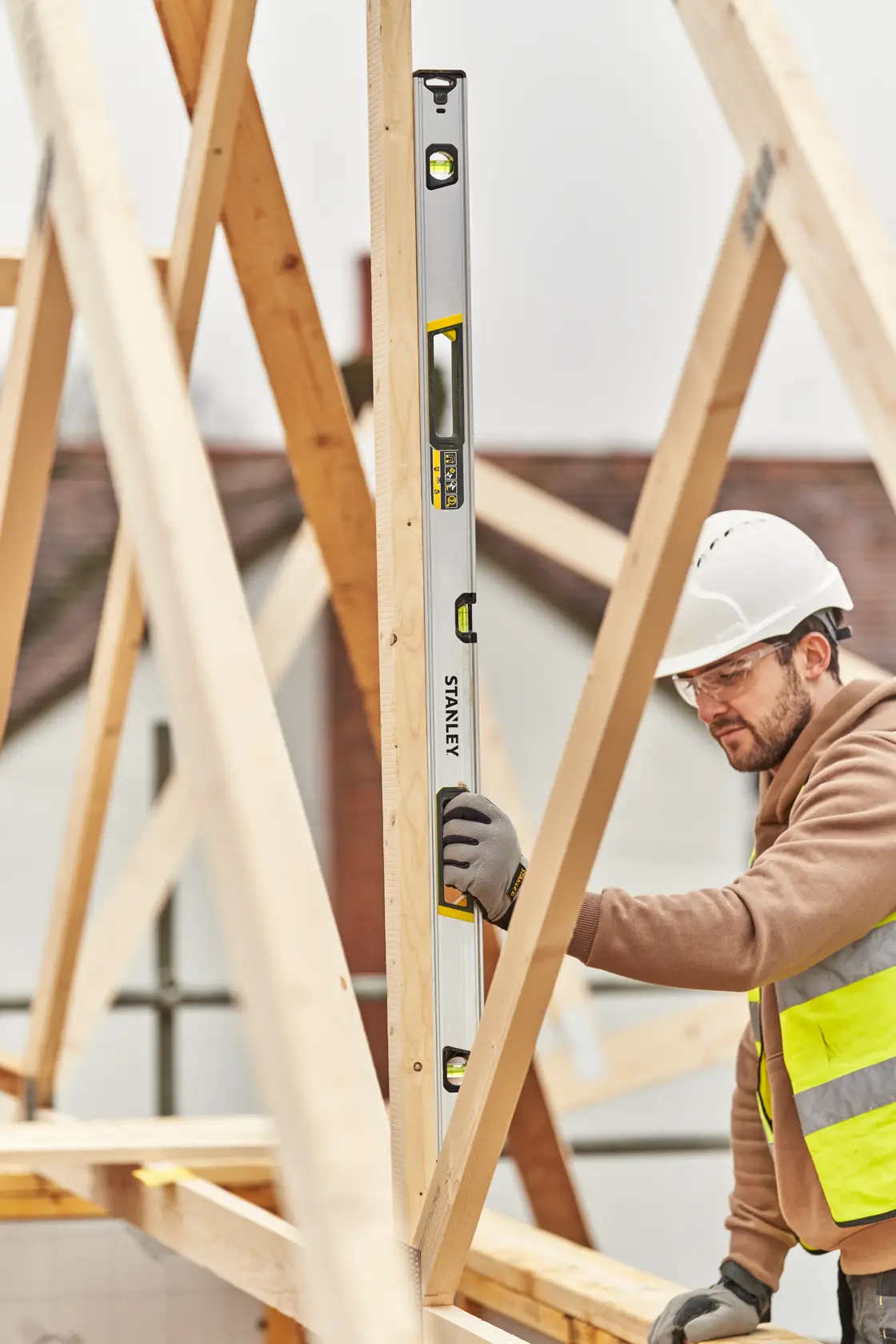 STANLEY FMHT43677 spirit level used vertically by a worker on wooden beams at a construction site.