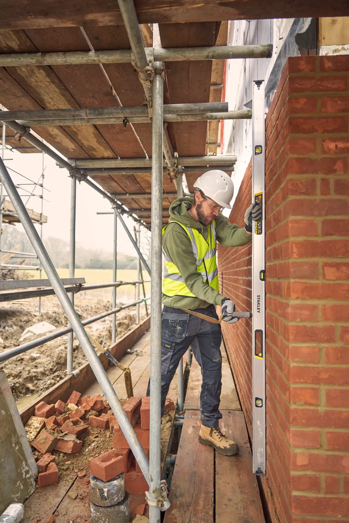 STANLEY FMHT43680-1 spirit level used by a construction worker checking a brick wall's alignment on scaffolding.