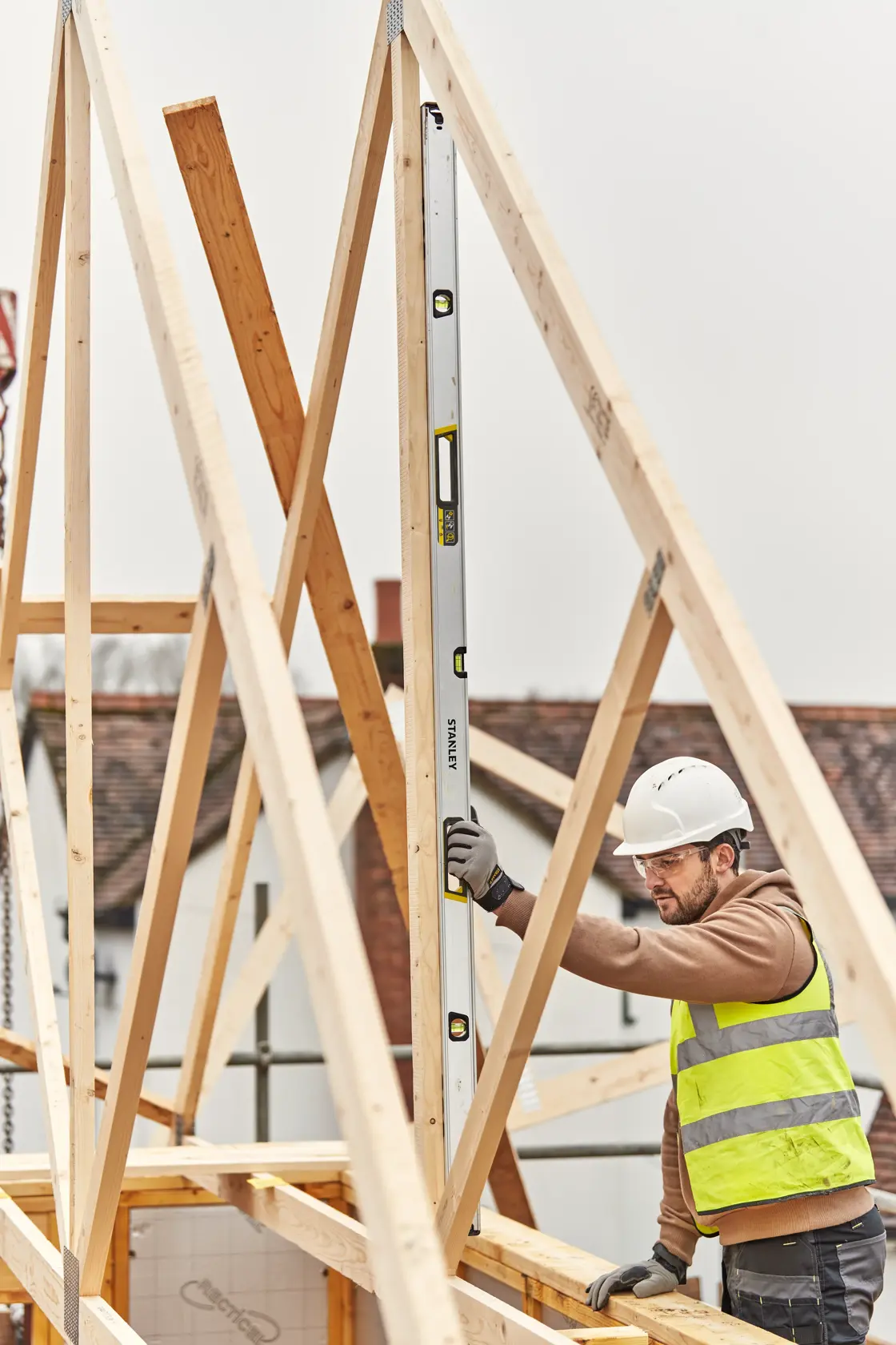 STANLEY FMHT43680-1 spirit level held vertically by worker at construction site with timber framing.