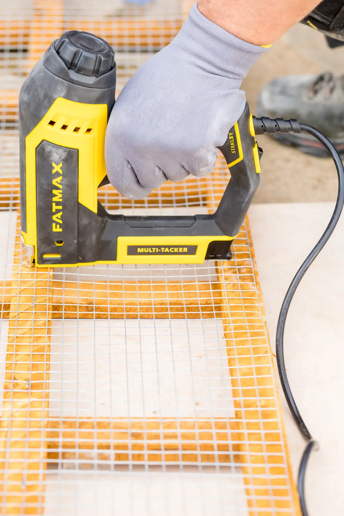 Photo of STANLEY FATMAX FMHT6-75934 electric multi-tacker stapling wire mesh to wood, close-up in use.