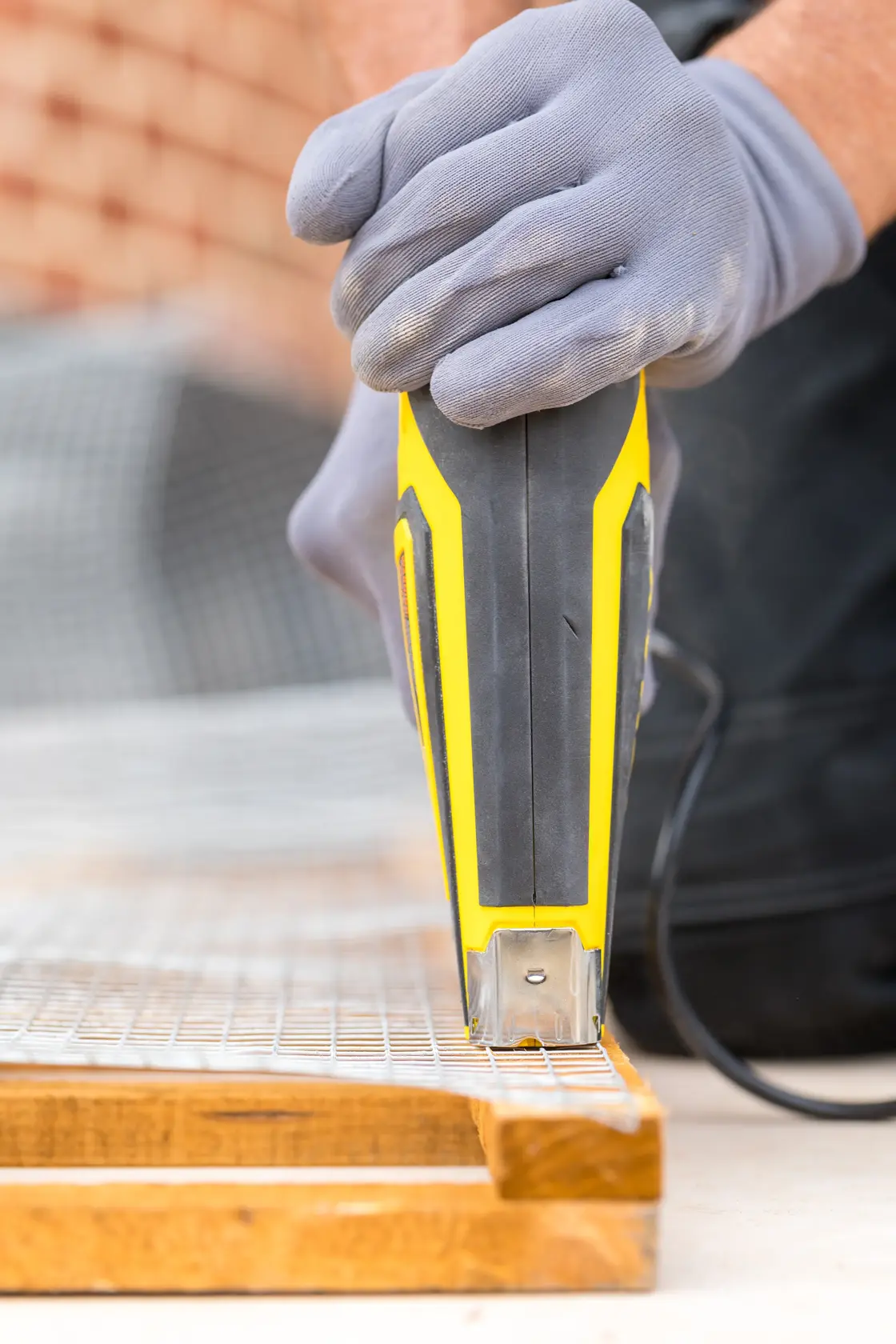 STANLEY FMHT6-75934 electric stapler close-up on wire mesh and wood, gloved hand operating tool.