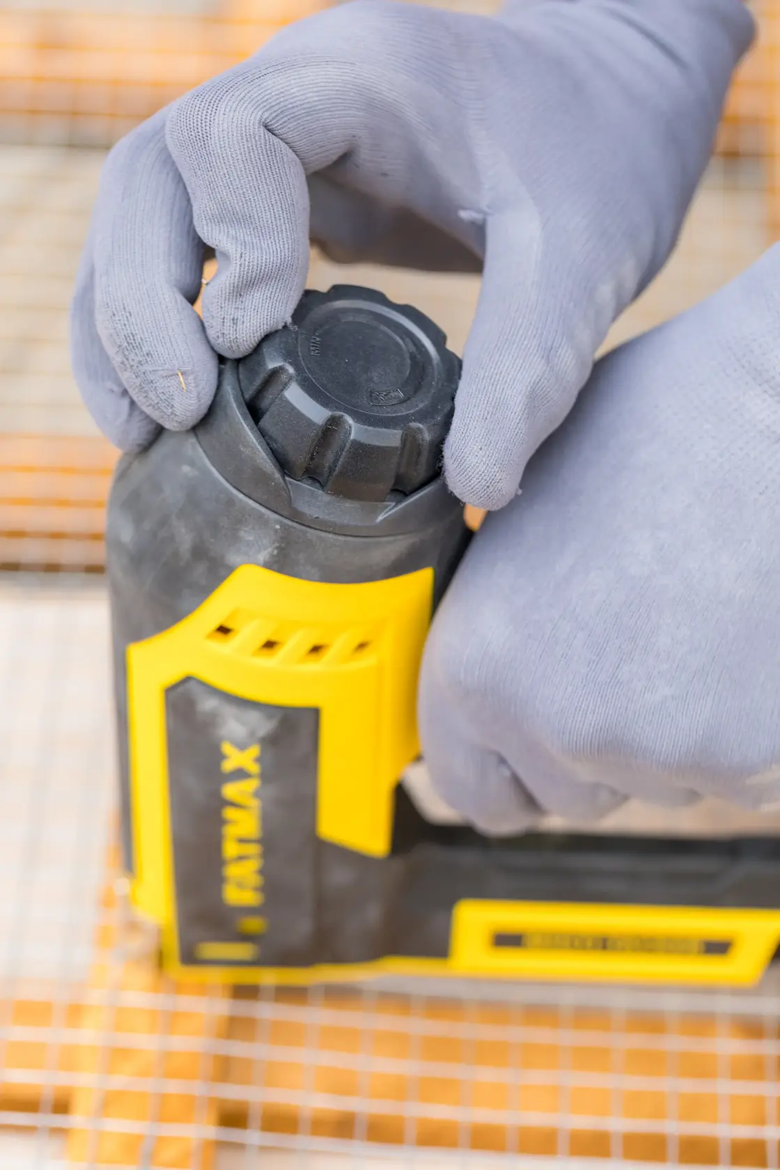 STANLEY FMHT6-75934 close-up photo of a person adjusting a yellow and black hand tool with gloved hands.
