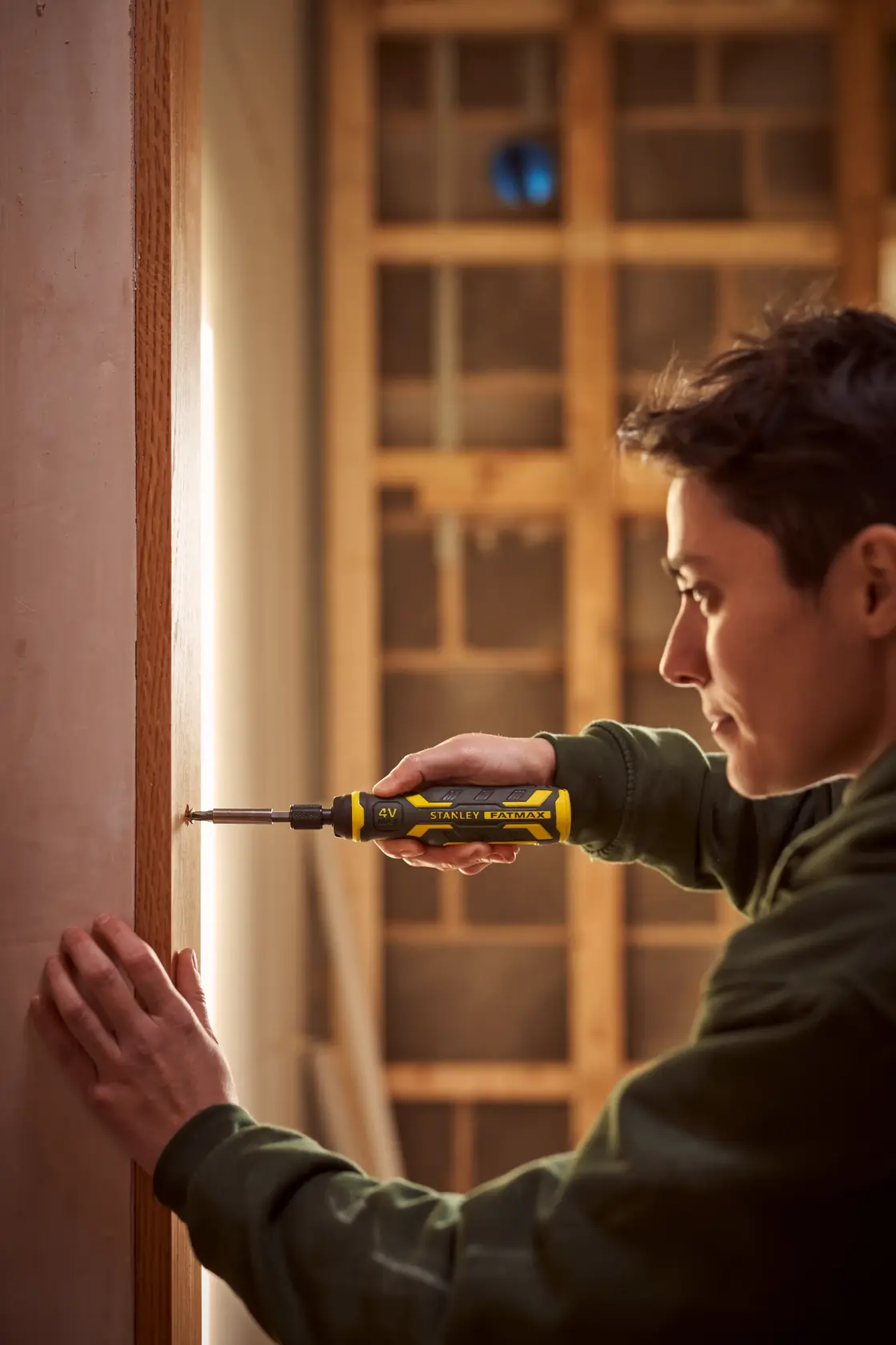 STANLEY FMHT66719-0 yellow cordless screwdriver held by person fixing screw in wooden frame.