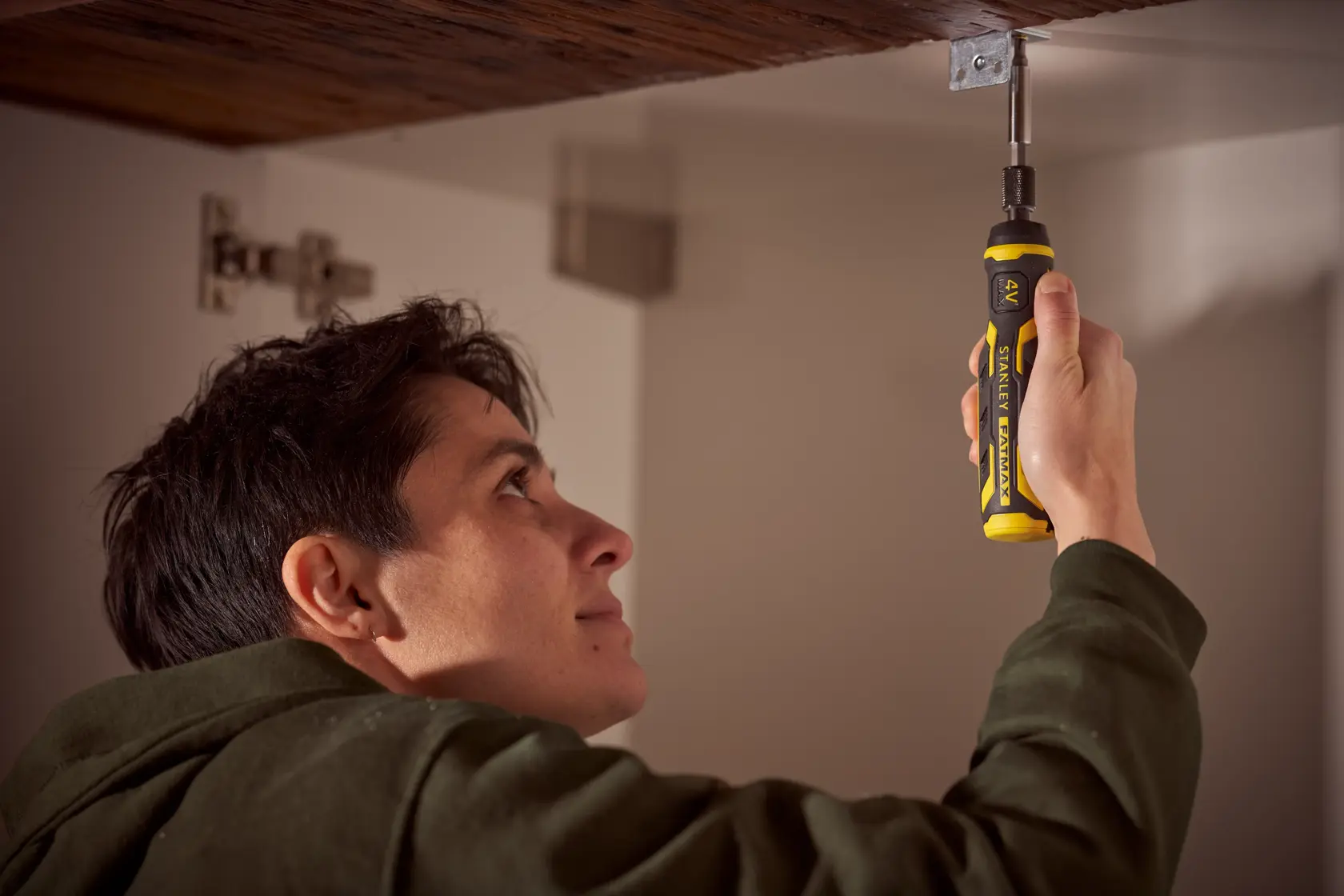 Person using STANLEY FMHT66719-0 ratcheting screwdriver under a wooden cabinet, yellow and black handle visible.