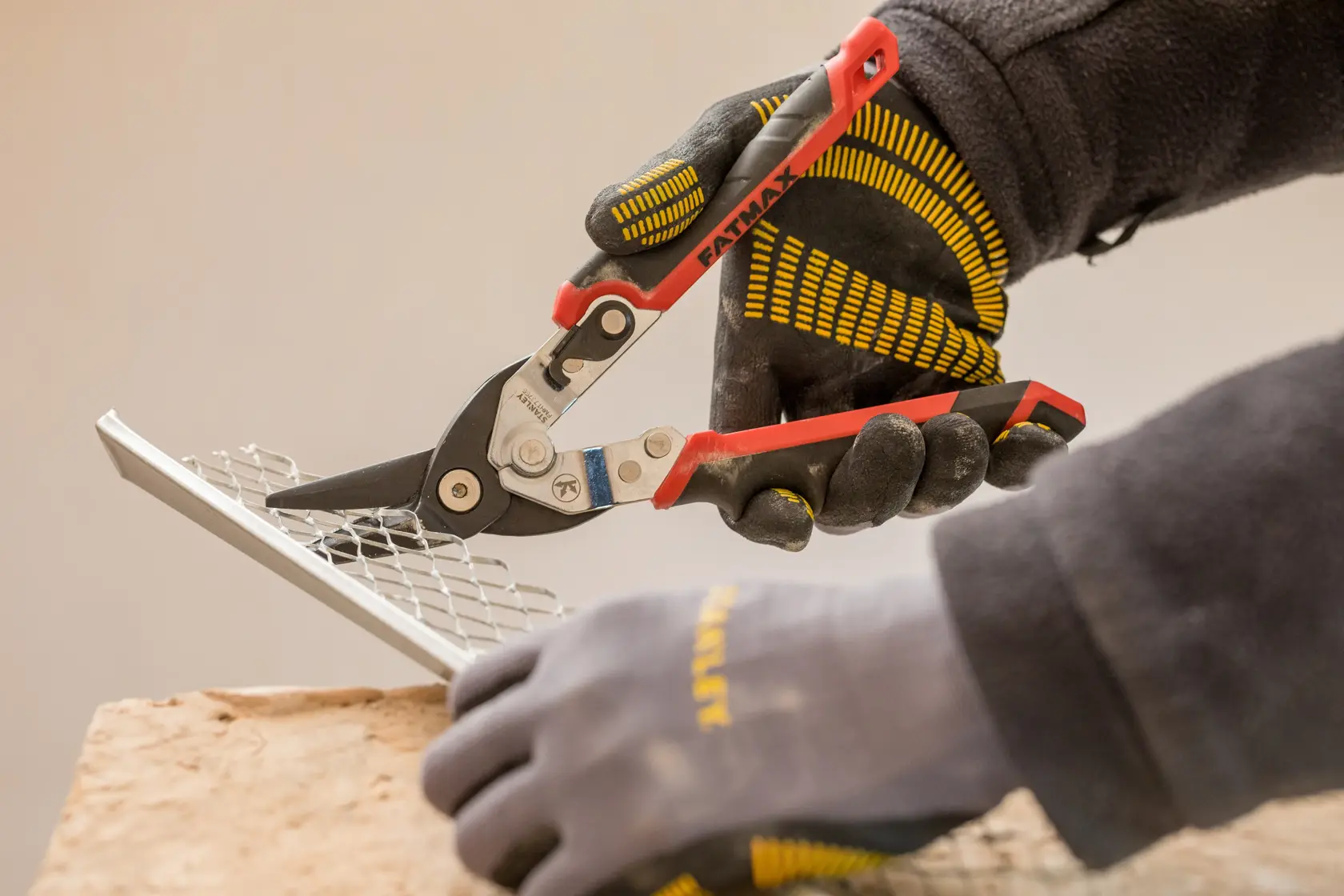 STANLEY FMHT73755 metal shears cutting mesh, close-up photo, worker wearing black and yellow gloves.