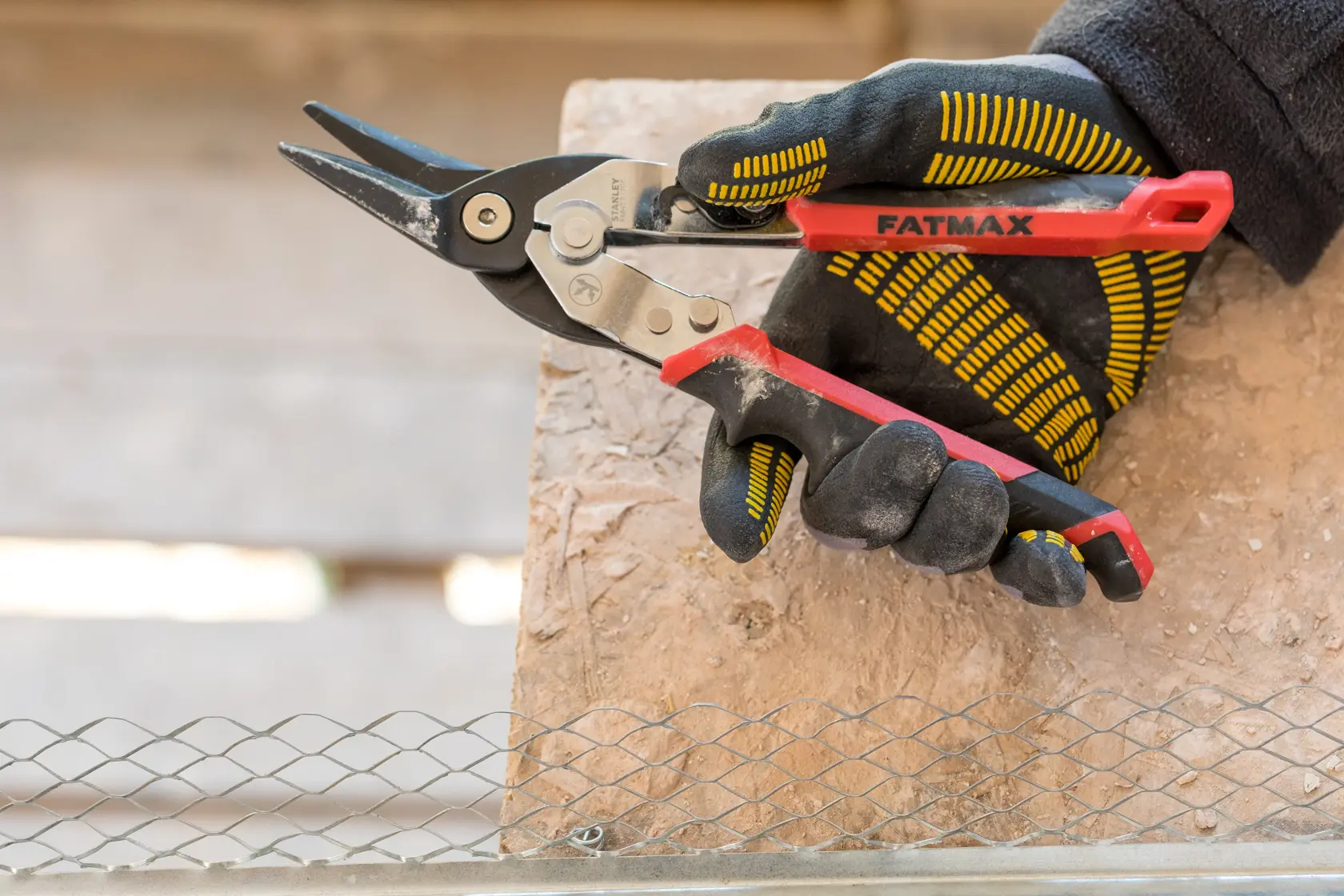 Stanley FMHT73755 metal snips with red handle in gloved hand, side angle, cutting wire mesh.