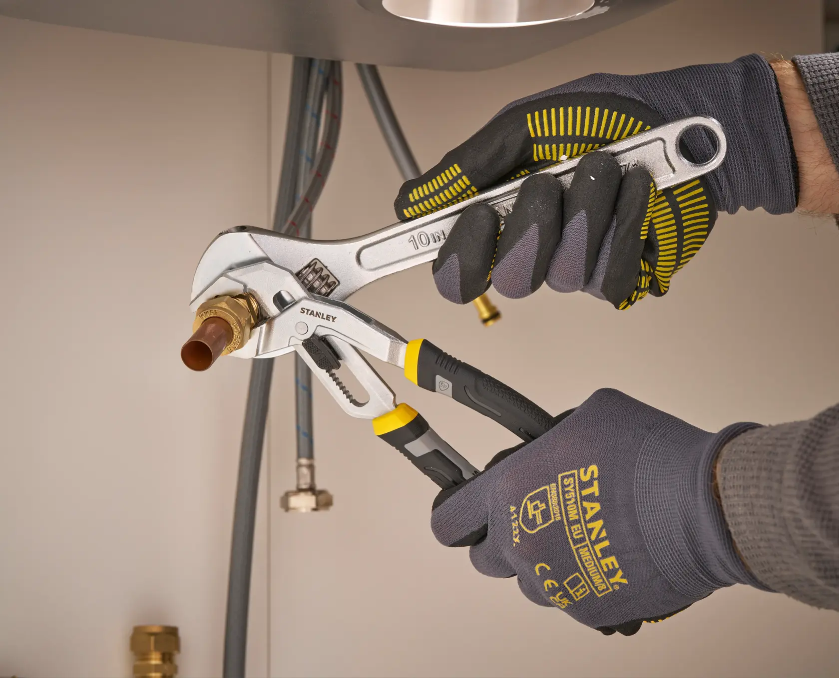 Stanley FMHT75508-0 adjustable wrench and pliers used on brass pipe fitting, close-up in plumbing work.