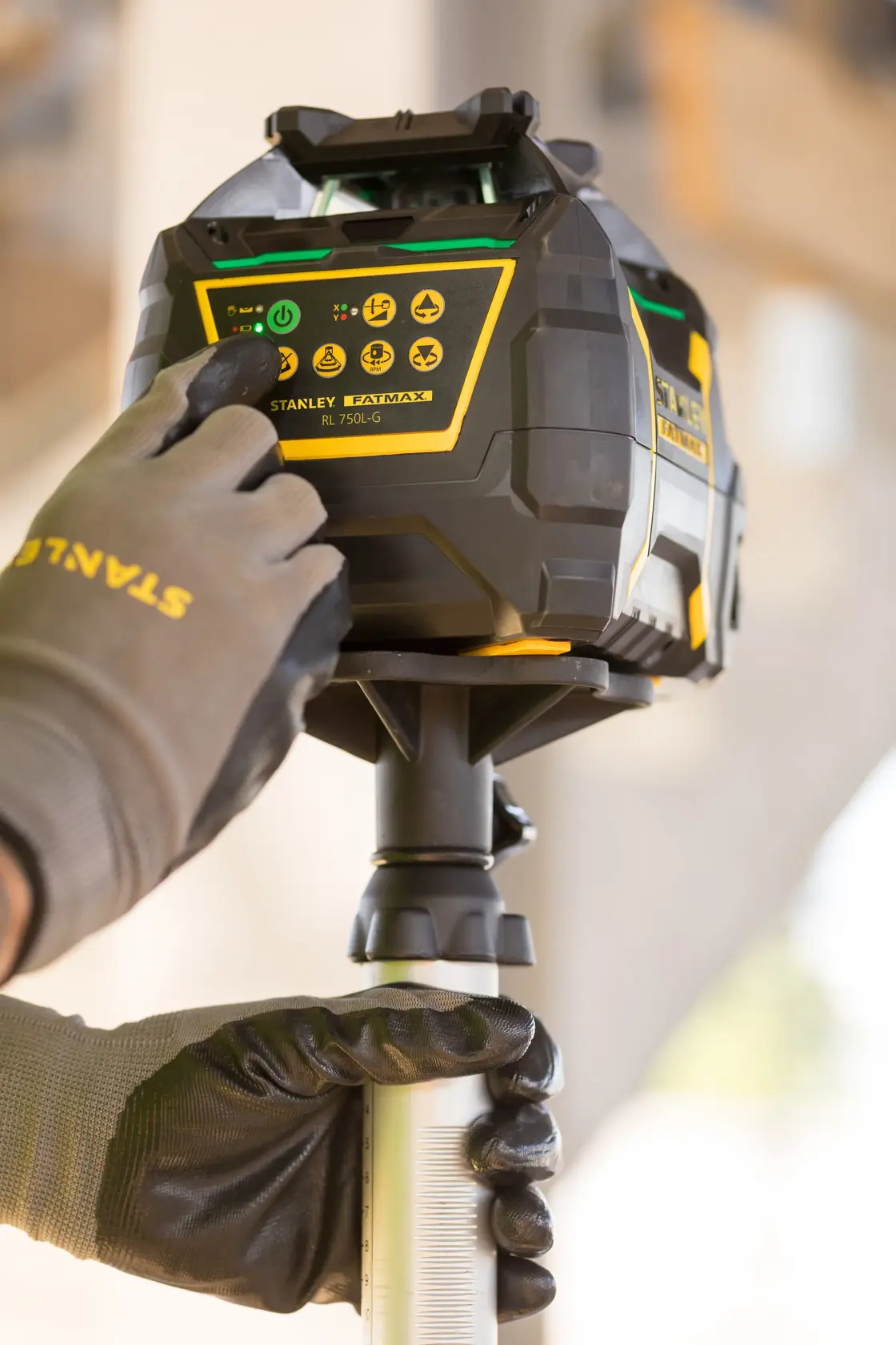 STANLEY FMHT77223-1 rotary laser level on tripod, close-up of control panel with gloved hand operating buttons.
