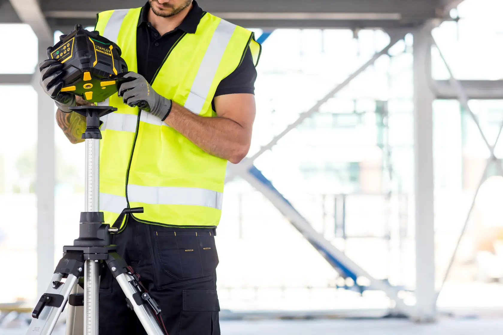 STANLEY FMHT77223-1 laser level on tripod, operator in hi-vis vest at construction site.