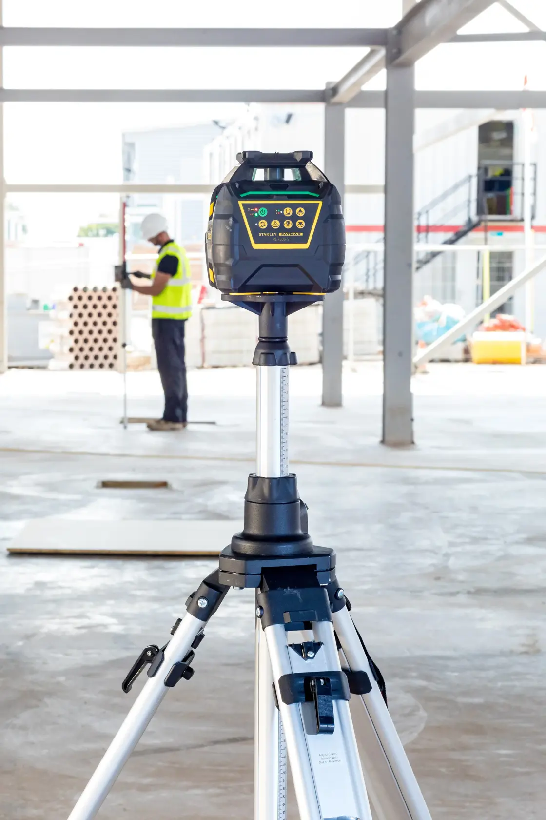 STANLEY FMHT77223-1 rotary laser level on tripod in construction site, with worker in background.