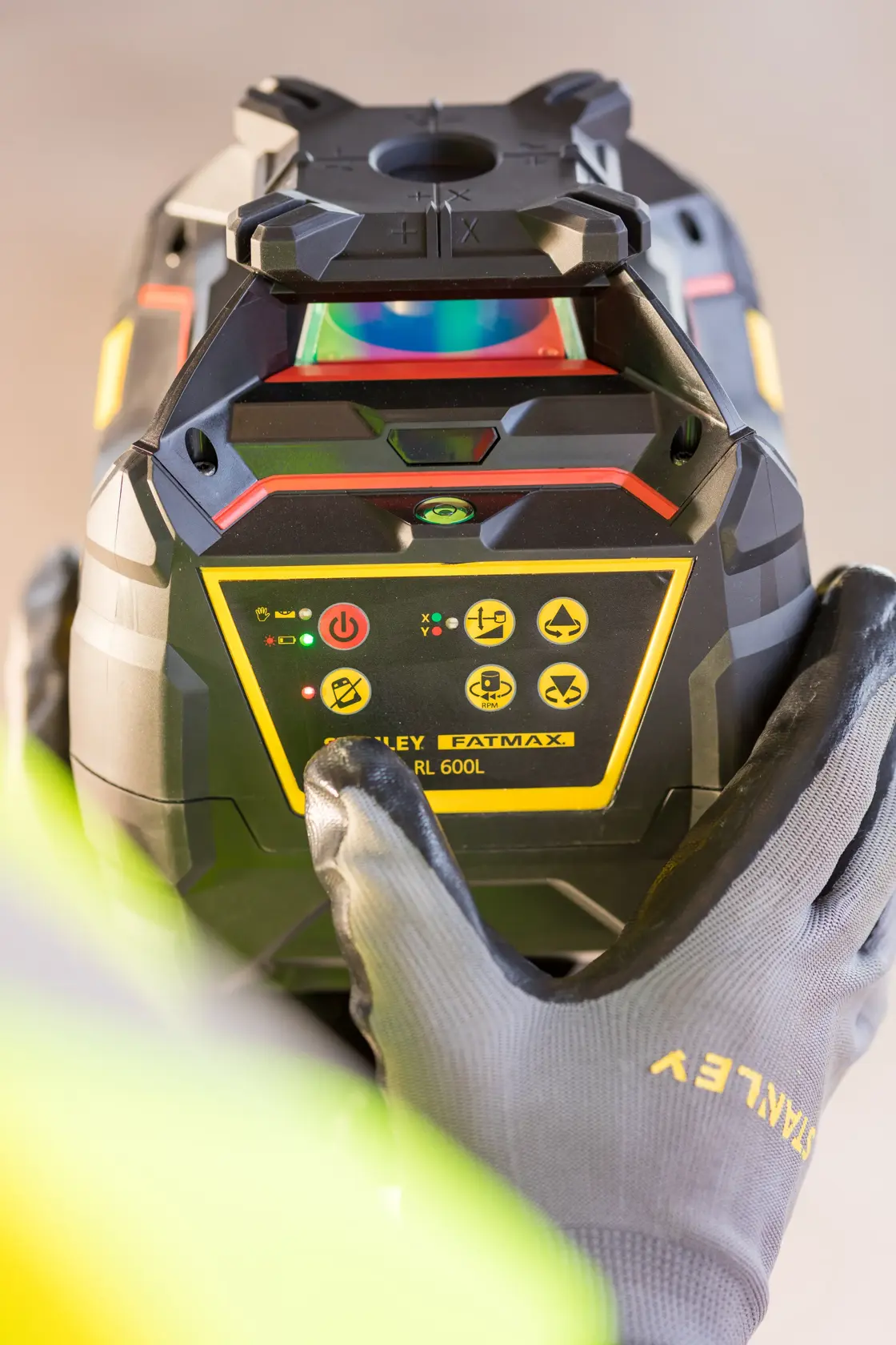 Photo of STANLEY FMHT77224-1 rotary laser level, close-up view of control panel with gloved hand adjusting settings.