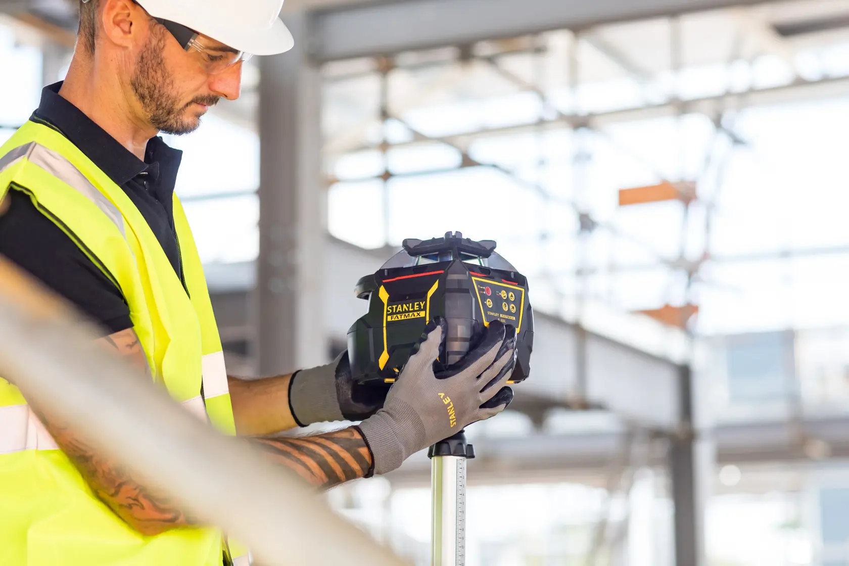 Photo of STANLEY FMHT77224-1 laser level on tripod, being adjusted by worker at construction site.